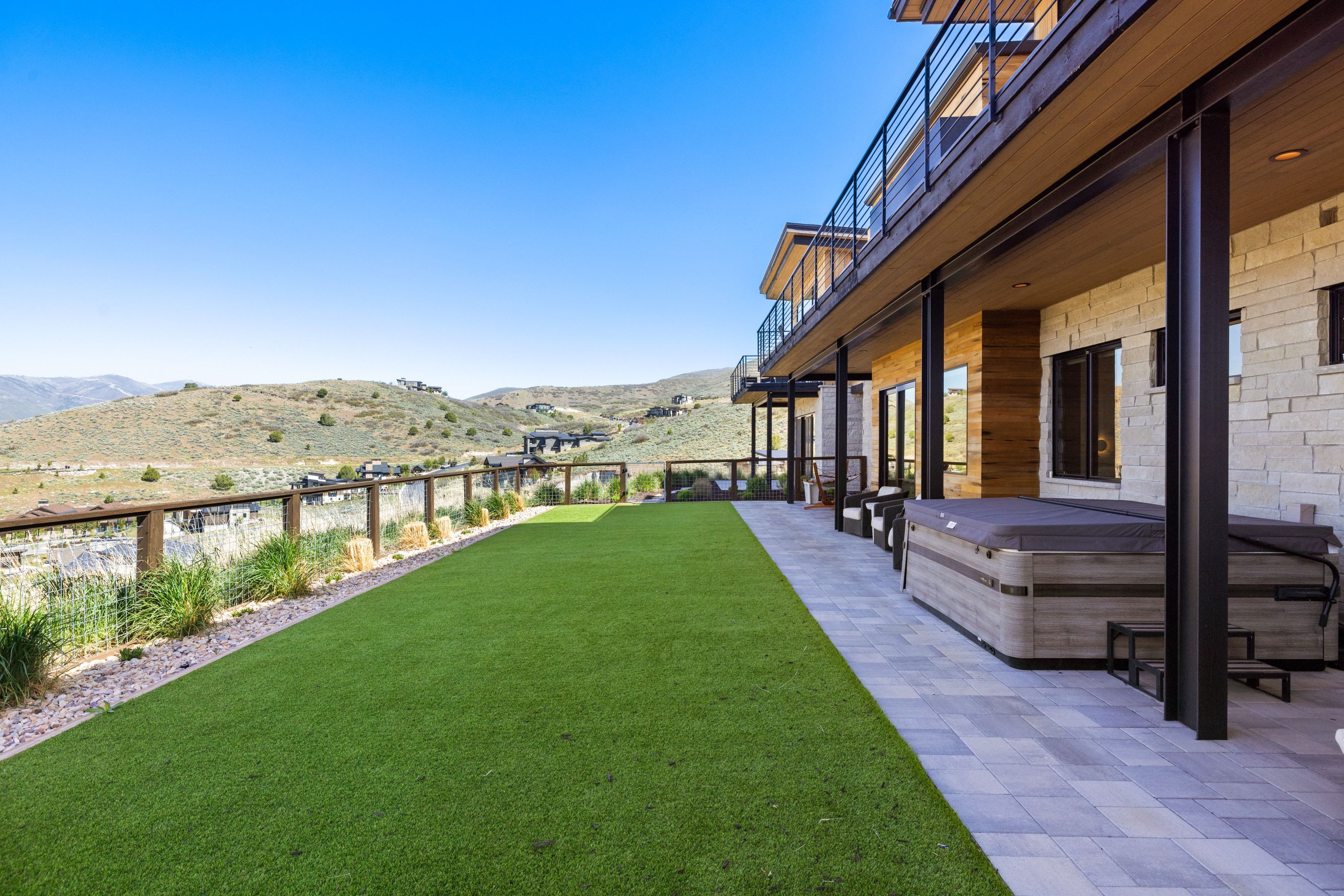 Lower-level patio featuring paver flooring, a built-in spa, and access to a fenced turf lawn