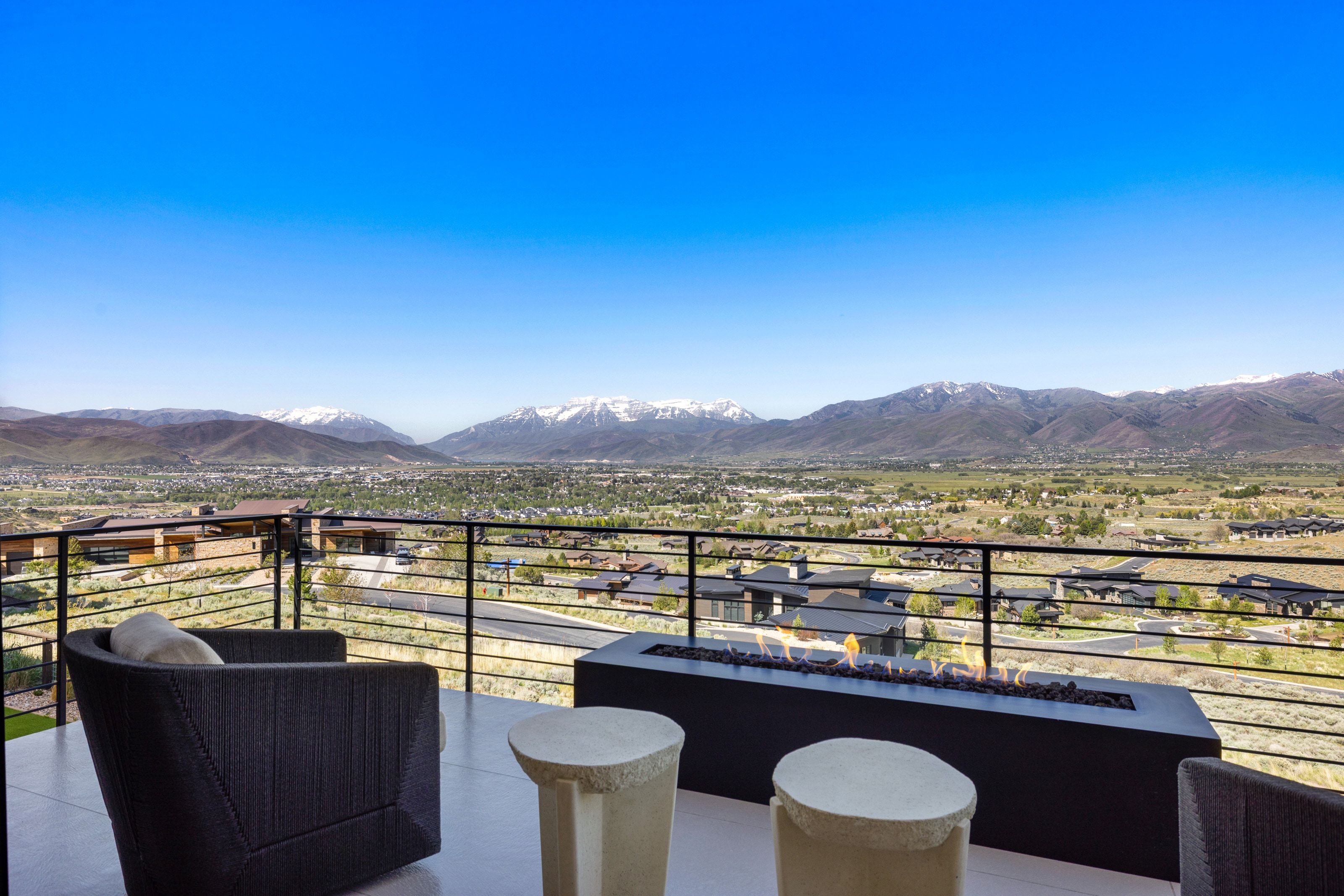 Outdoor patio featuring a modern fire feature, glass railing, and snow-capped mountain scenery