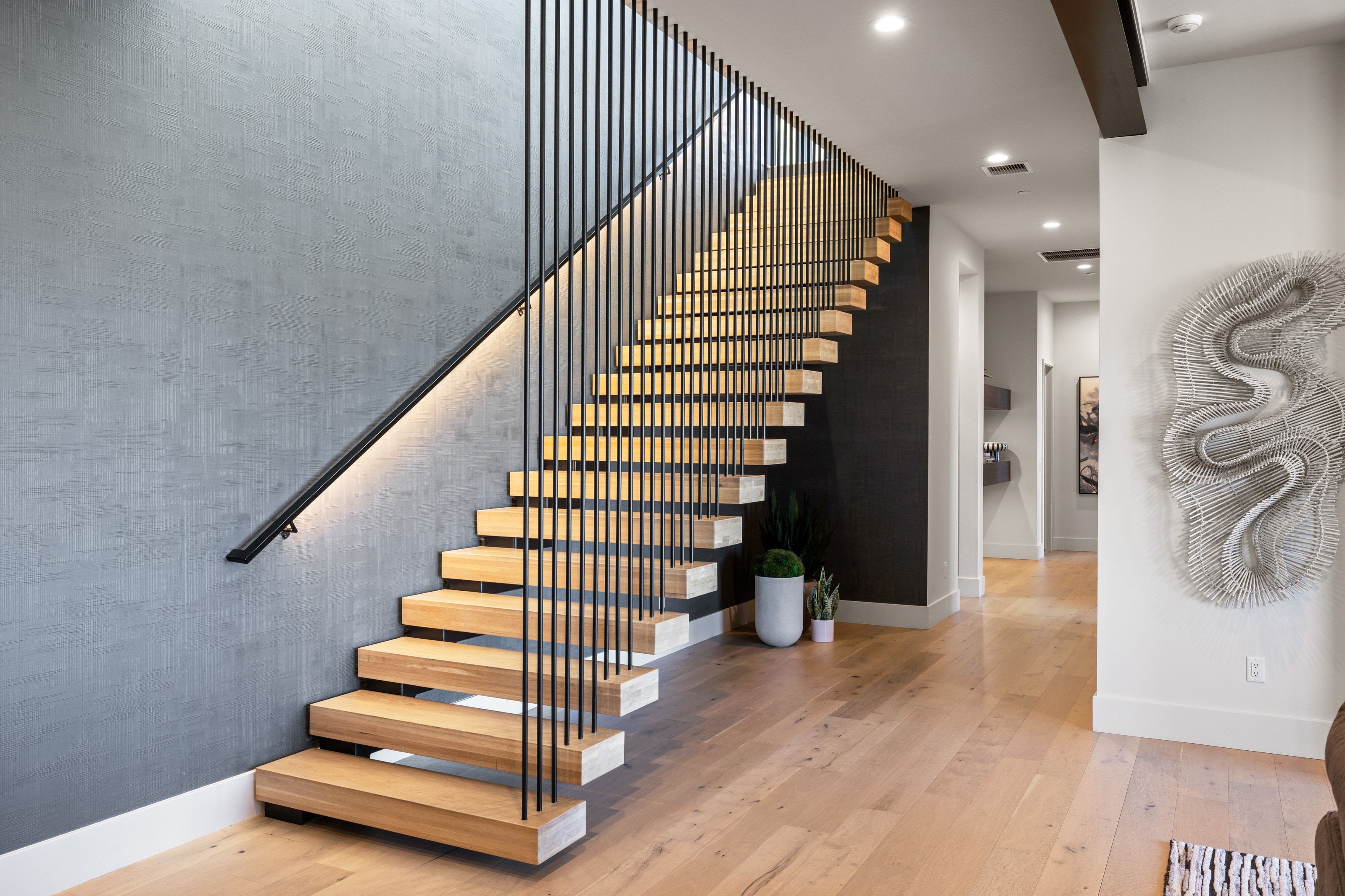 Floating staircase with light wood-finish treads, black vertical balusters, and an illuminated black handrail