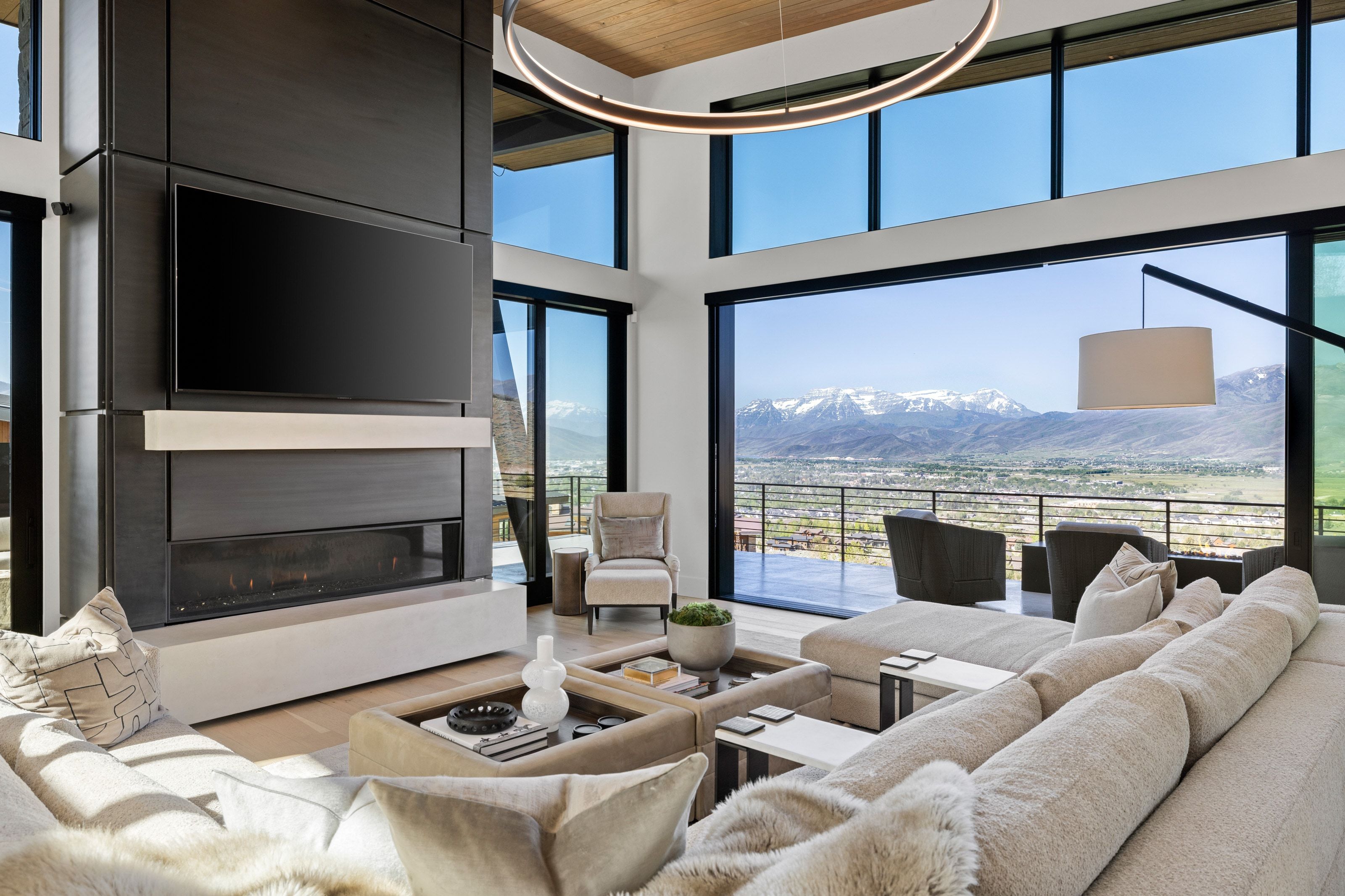 Spacious living area featuring a contemporary fireplace with a built-in media center, floor-to-ceiling windows, and sliding glass doors opening to an exterior balcony