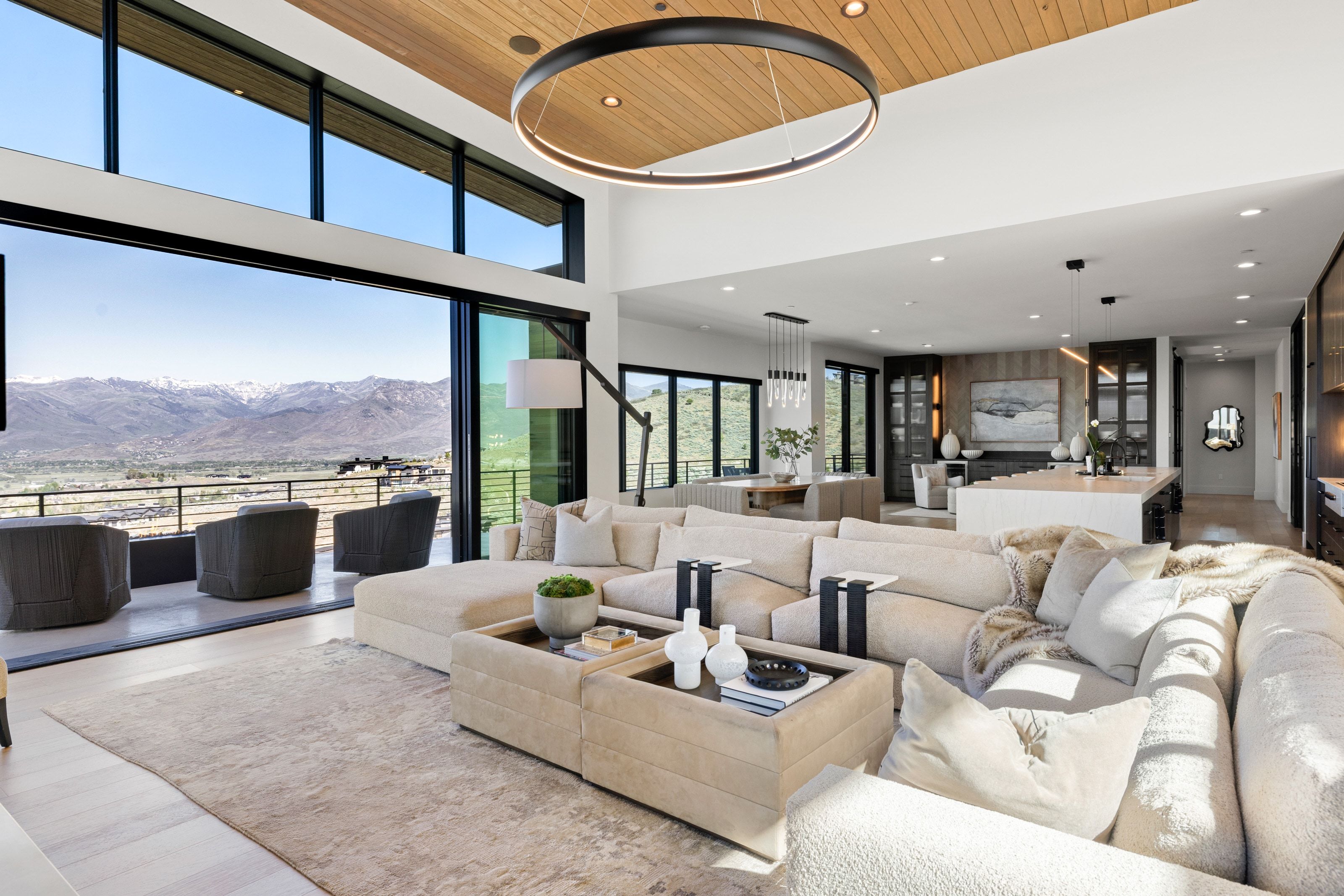 Spacious living area featuring expansive glass sliding doors, wood-finish flooring, a vaulted ceiling with wood paneling, and an integrated kitchen with a large island