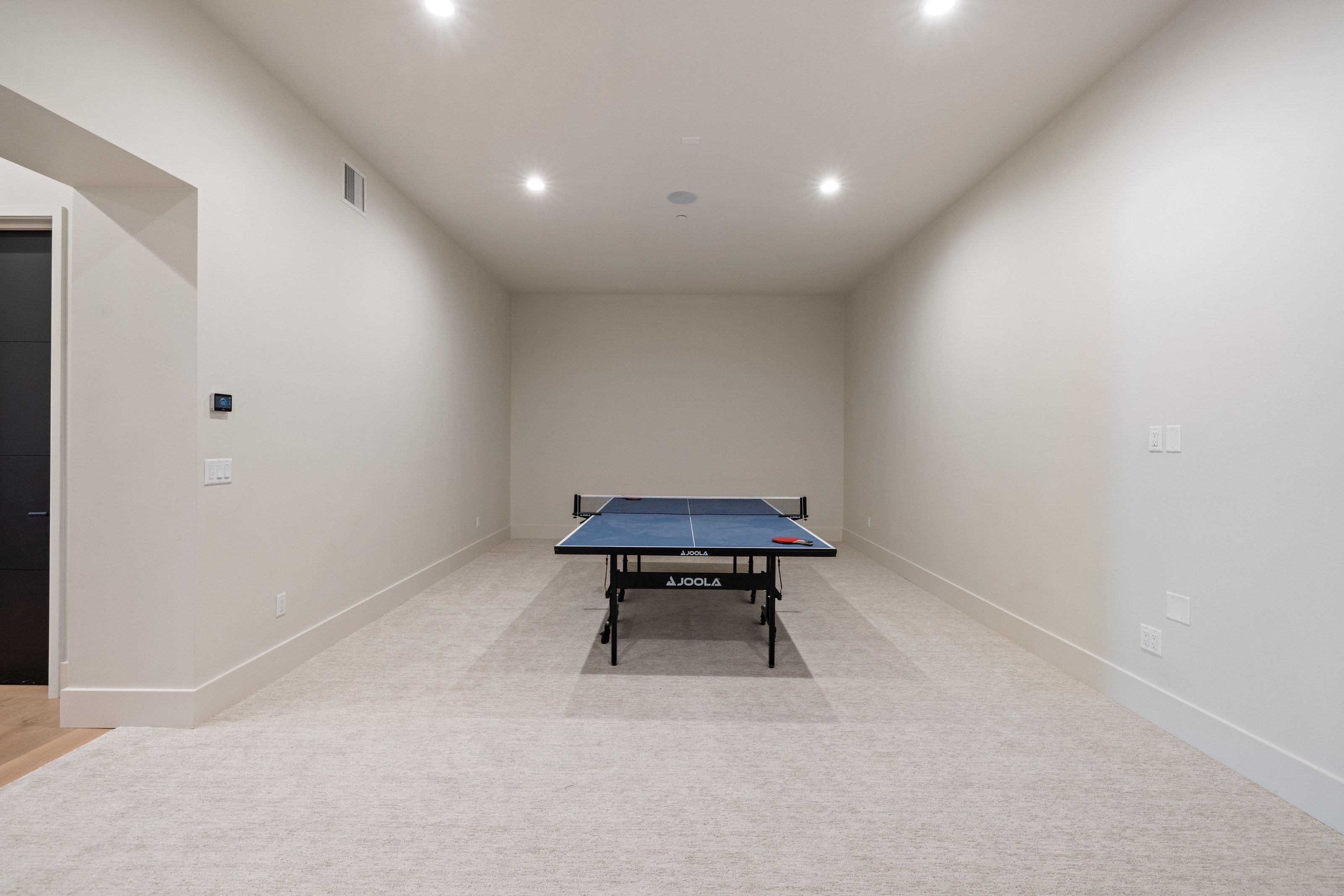 Spacious room featuring light-toned carpeting, recessed ceiling lighting, and a dark interior door with sleek hardware