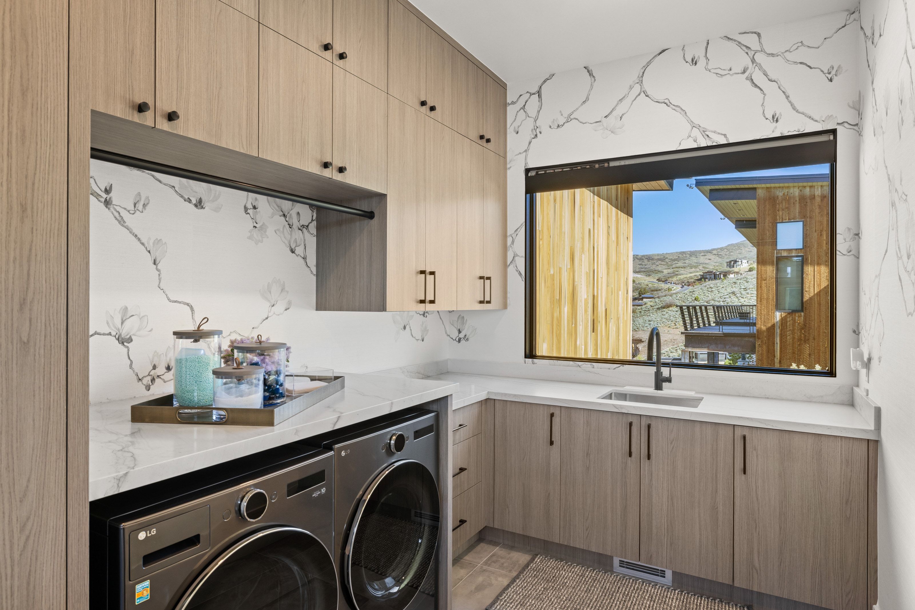 Laundry room featuring light wood-finish cabinetry, white countertops, built-in sink with a matte black faucet, and a large window
