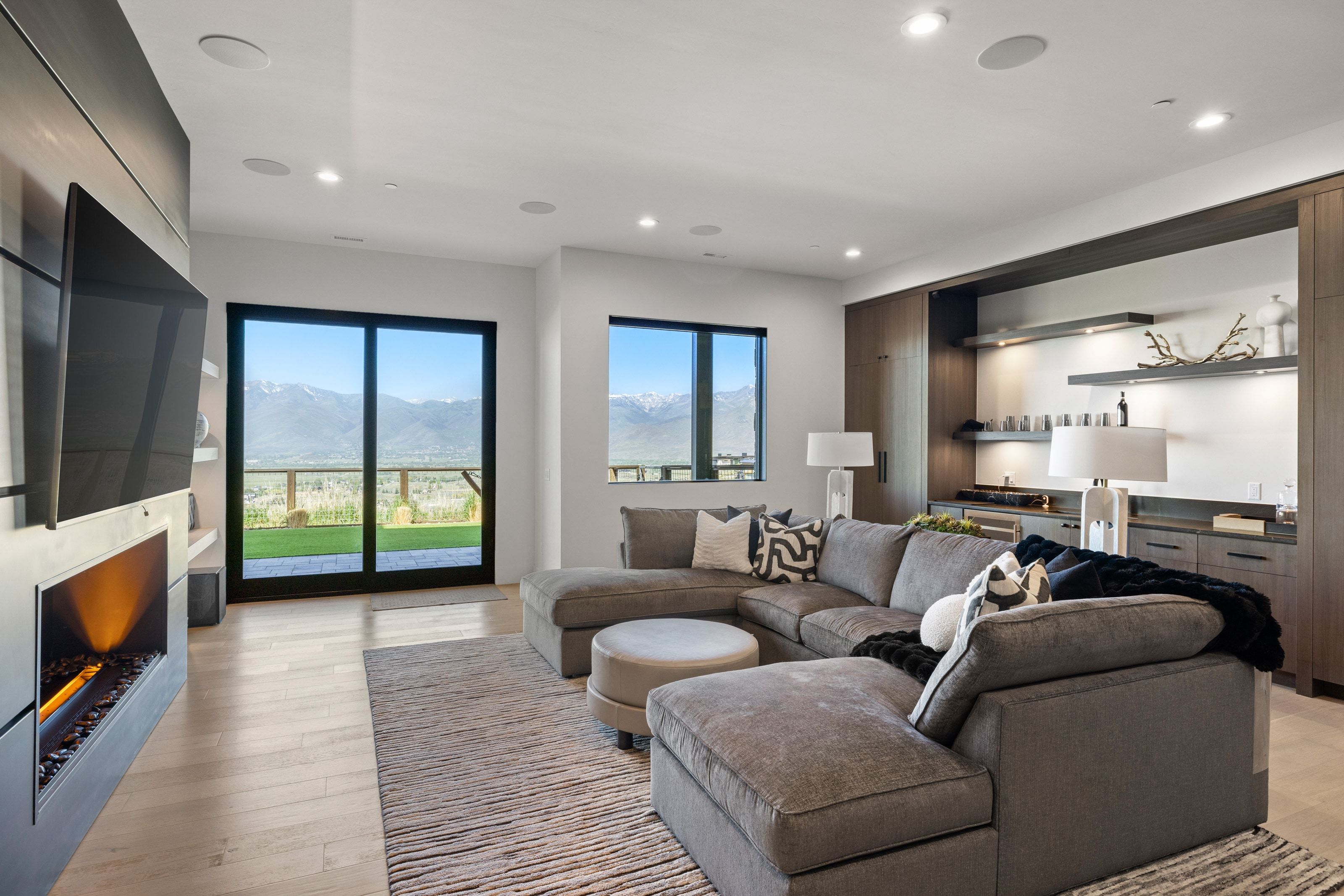 Open-concept living space featuring a built-in linear fireplace, wood-finish flooring, recessed lighting, and a built-in wet bar with shelving