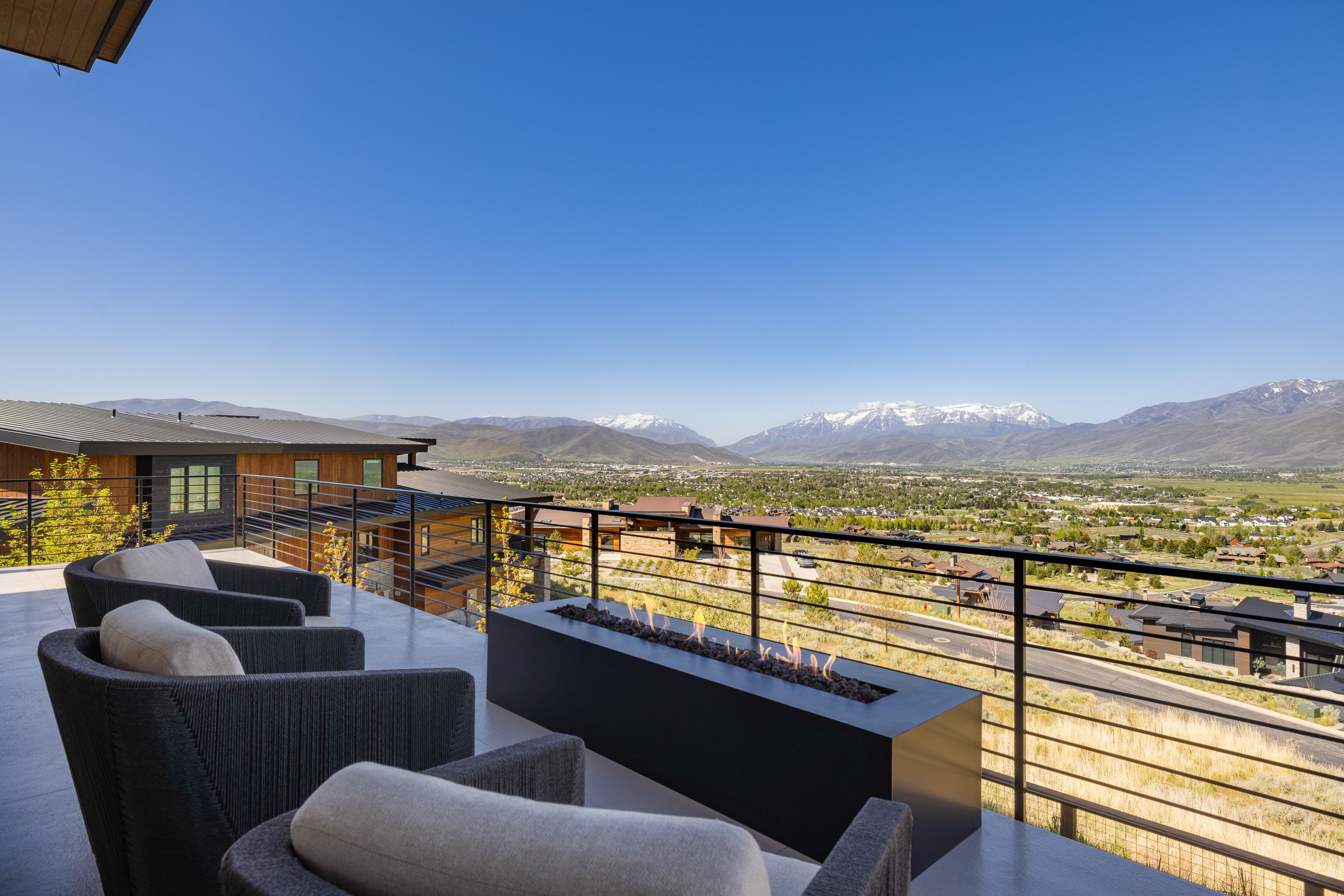Expansive outdoor patio with a linear fire feature, dark-toned horizontal railing, and a clear mountain backdrop