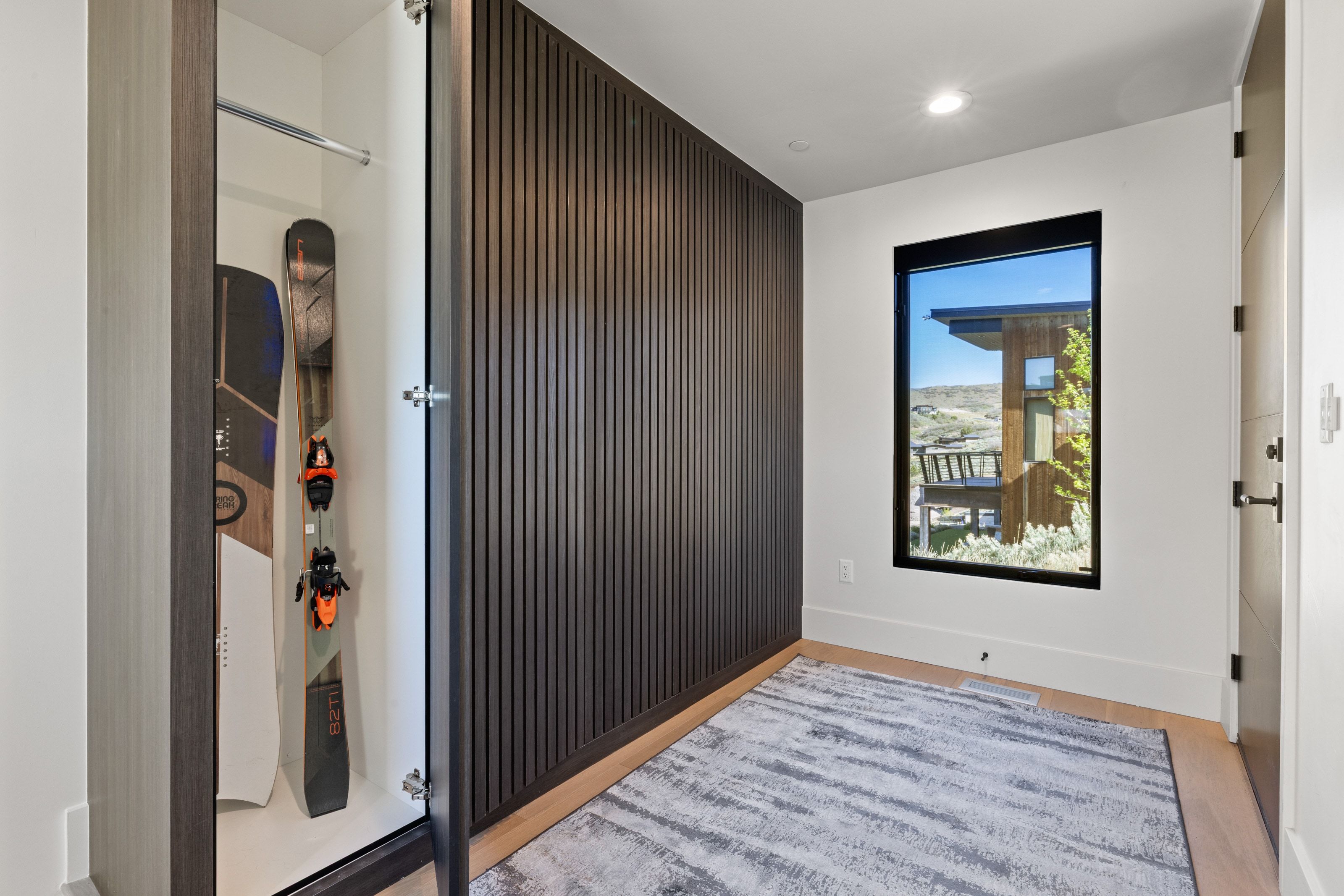 Entryway featuring a floor-to-ceiling slatted accent wall, a built-in storage closet, wood-finish flooring, a contemporary window with a black frame, and recessed lighting