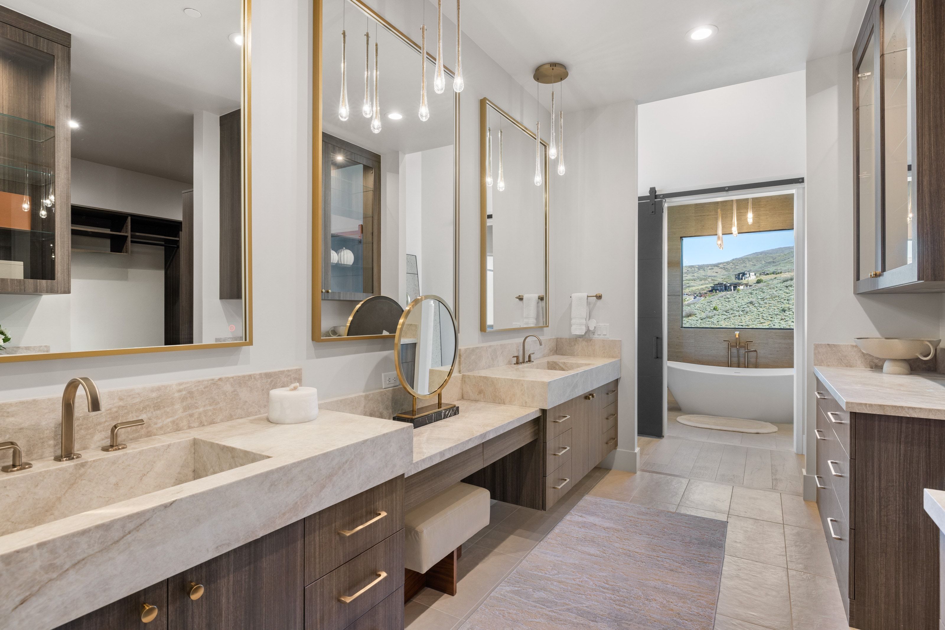 Dual vanity with integrated stone sinks, custom dark wood-finish cabinetry, and gold-framed mirrors