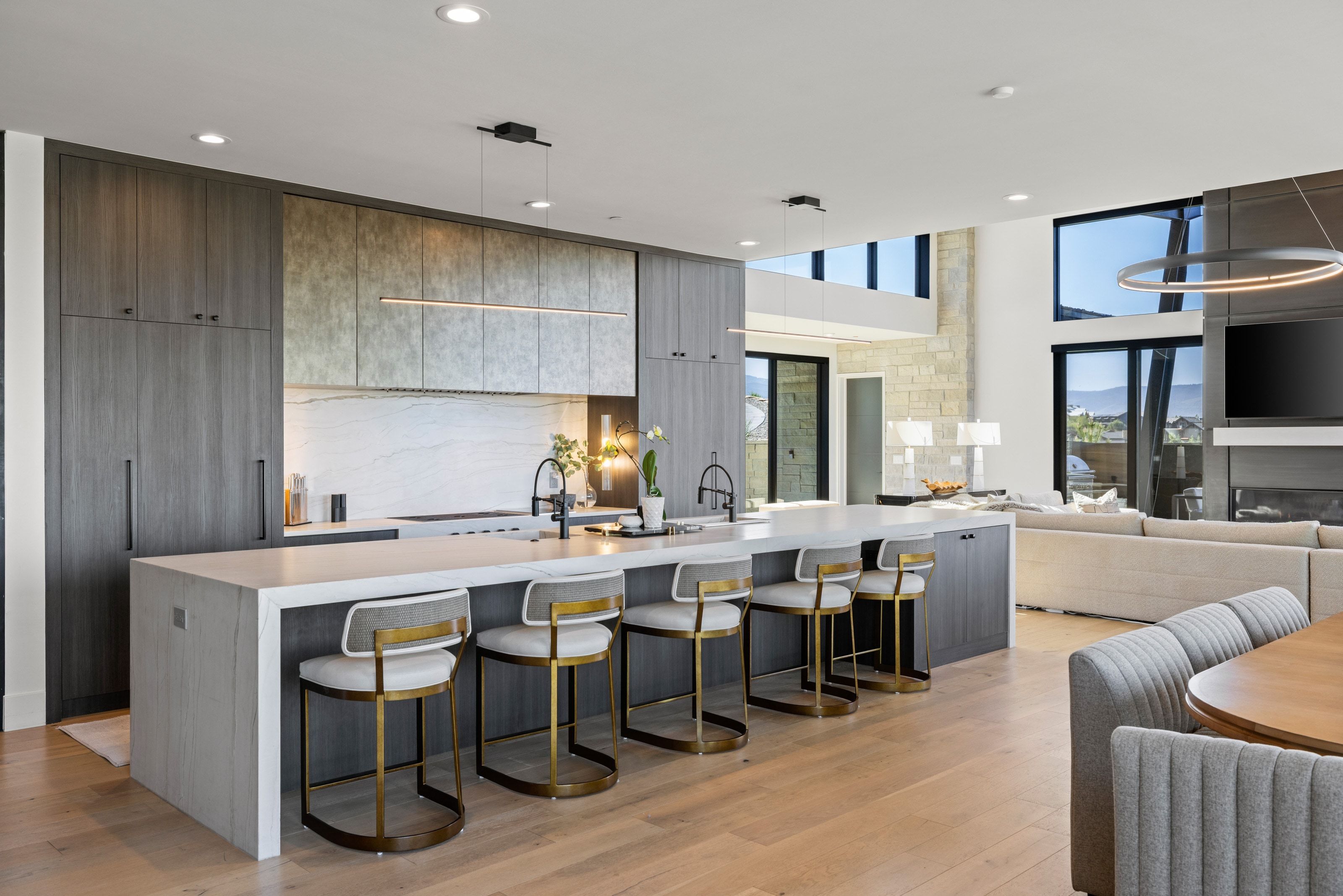 Open-concept kitchen with a large waterfall island, integrated appliances, and a full-height stone backsplash