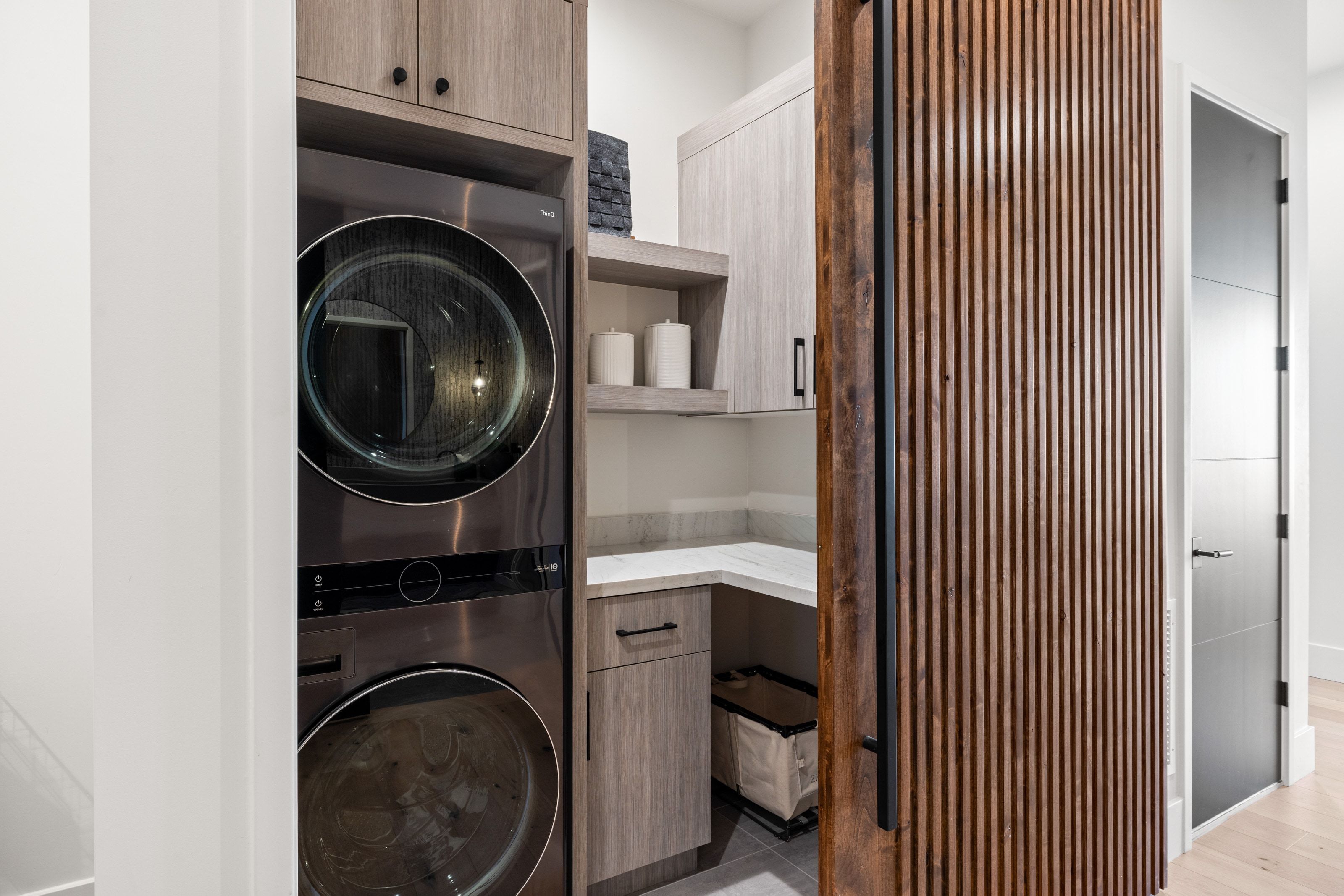 Laundry area featuring stacked appliances, wood-finish cabinetry, open shelving, and a light-colored countertop