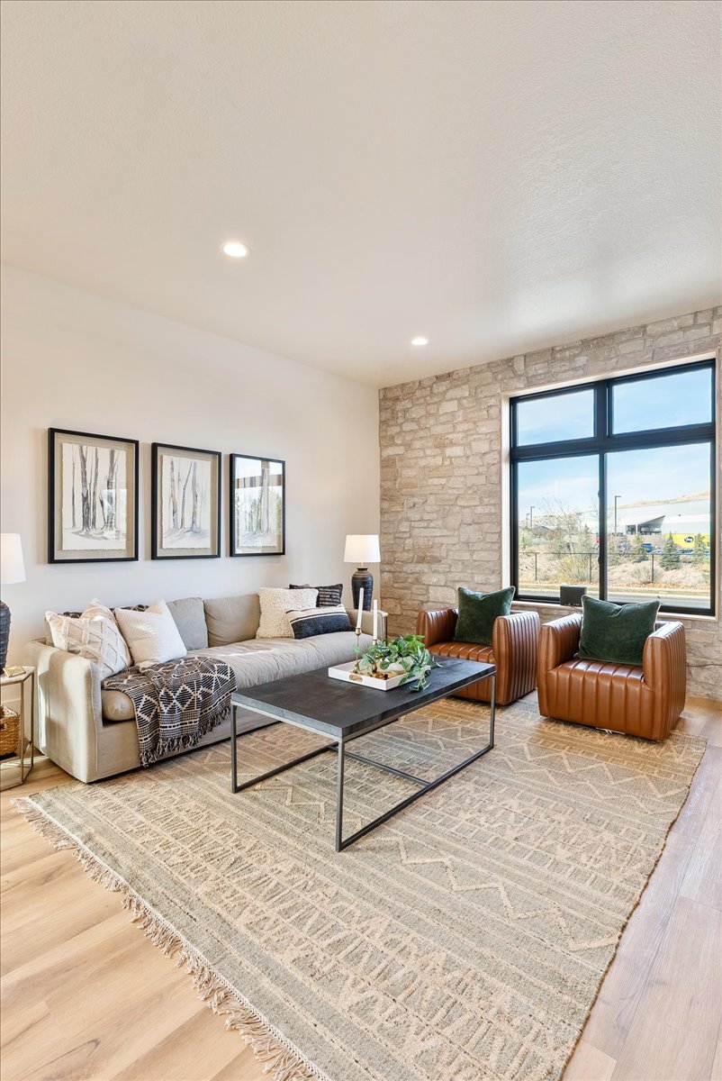 Spacious living area featuring light wood-finish flooring, a prominent stone accent wall, and a large multi-pane window