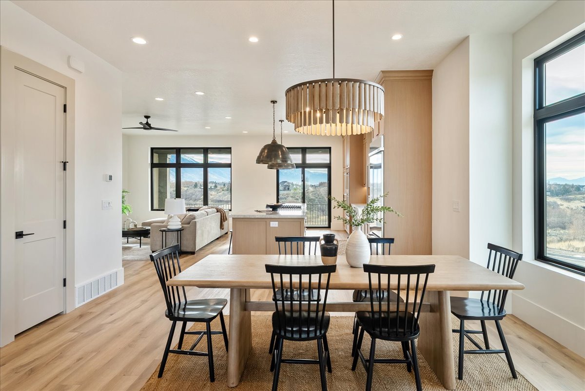 Open-concept dining area featuring wood-finish flooring, a contemporary chandelier, a light wood dining table, and large black-framed windows
