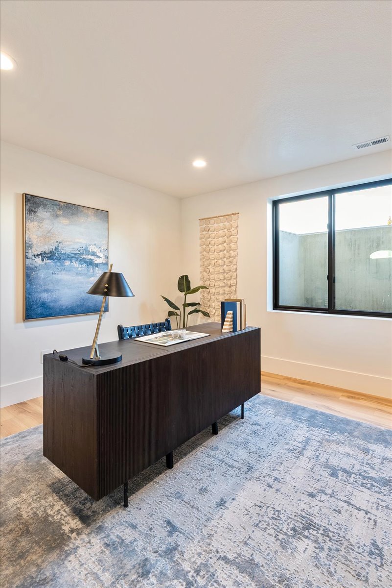 Dedicated office space featuring light wood-finish flooring, recessed lighting, and a black-framed window