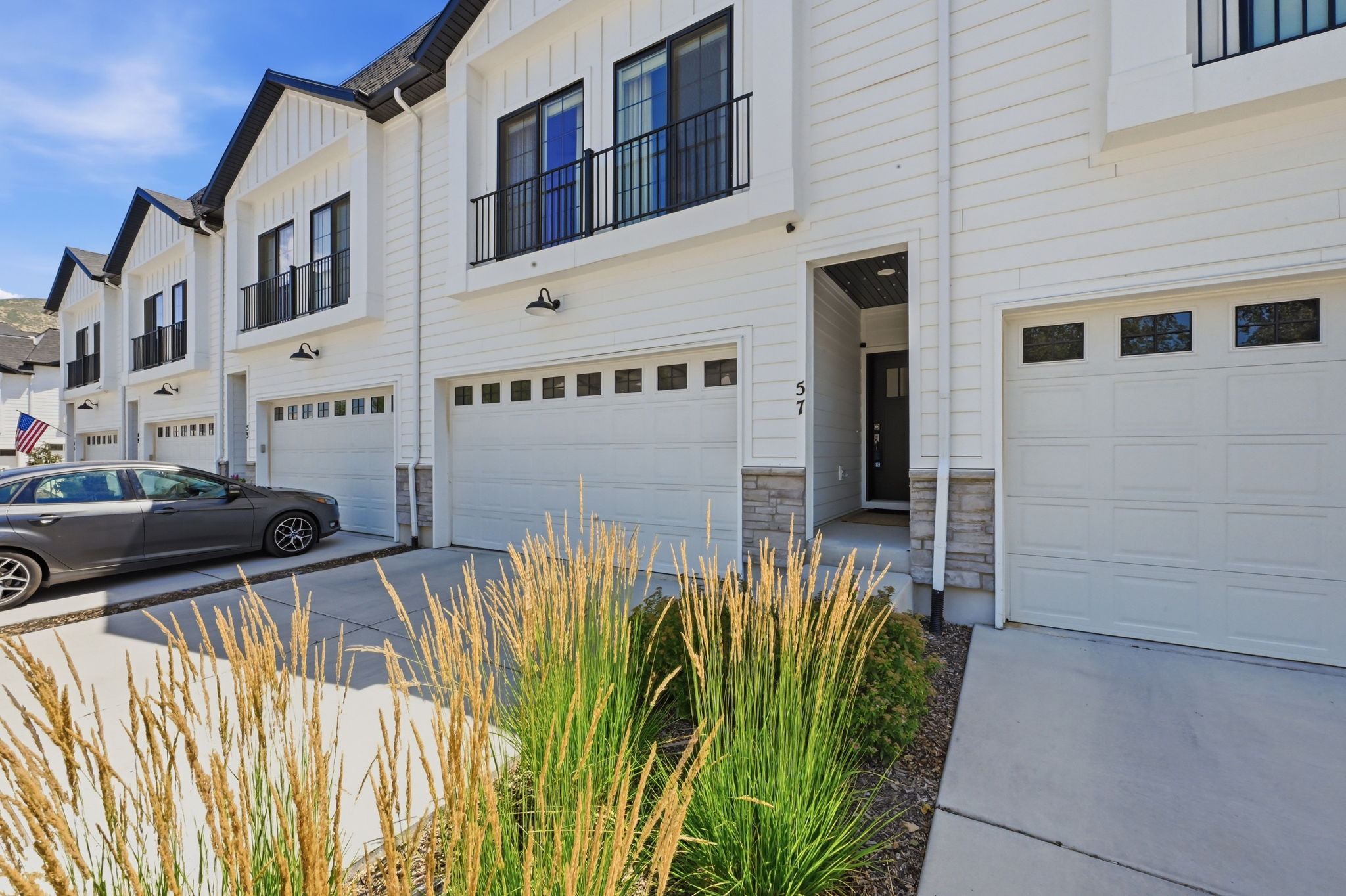 Contemporary townhome exterior featuring white siding, black trim accents, a double-car garage with transom windows, and a prominent front entry