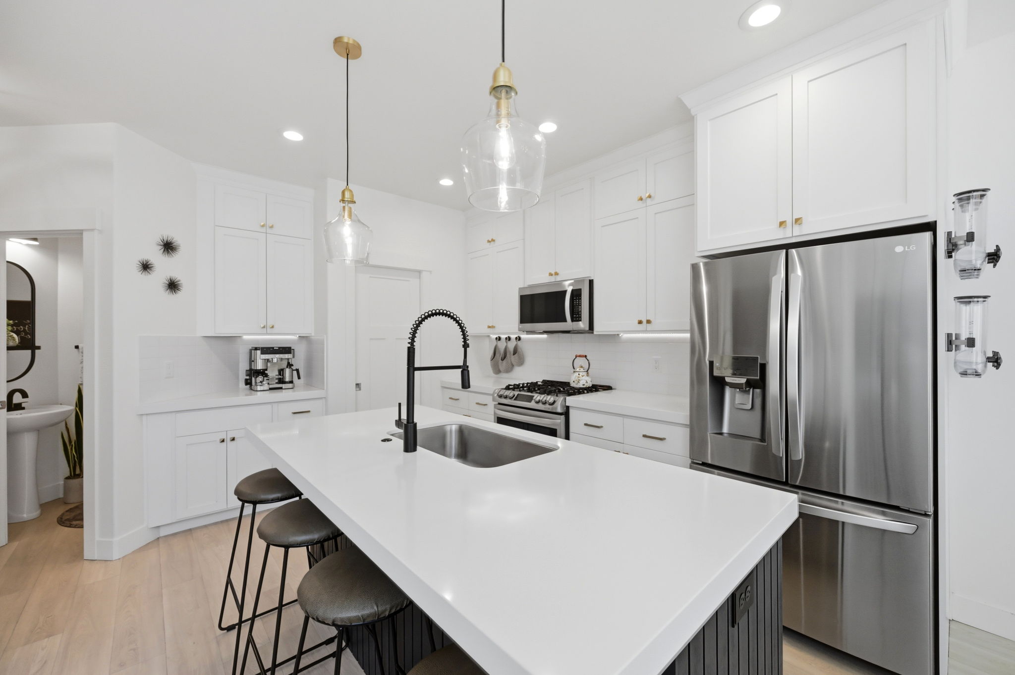 Kitchen featuring a large island with an undermount sink and matte black faucet, white shaker-style cabinetry with brass-finish hardware, stainless steel appliances