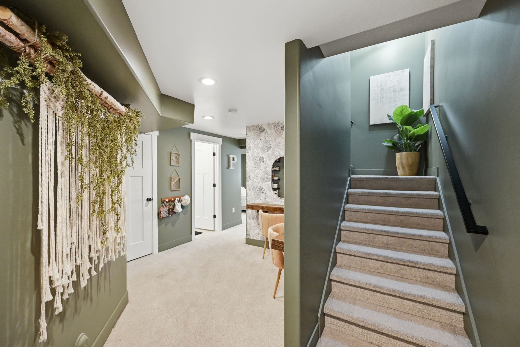 Carpeted staircase with black metal handrail leading to a hallway with recessed lighting