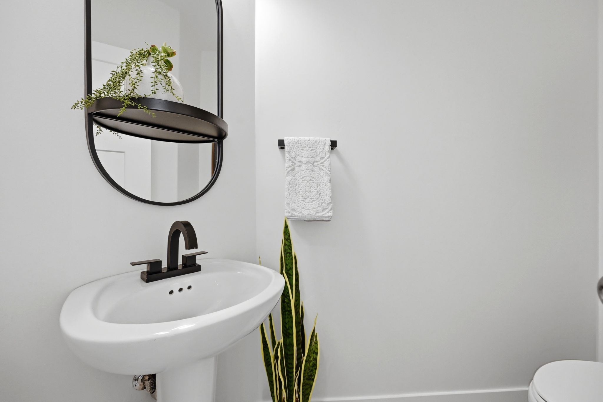 Pedestal sink with a matte black faucet and coordinating oval mirror featuring an integrated shelf