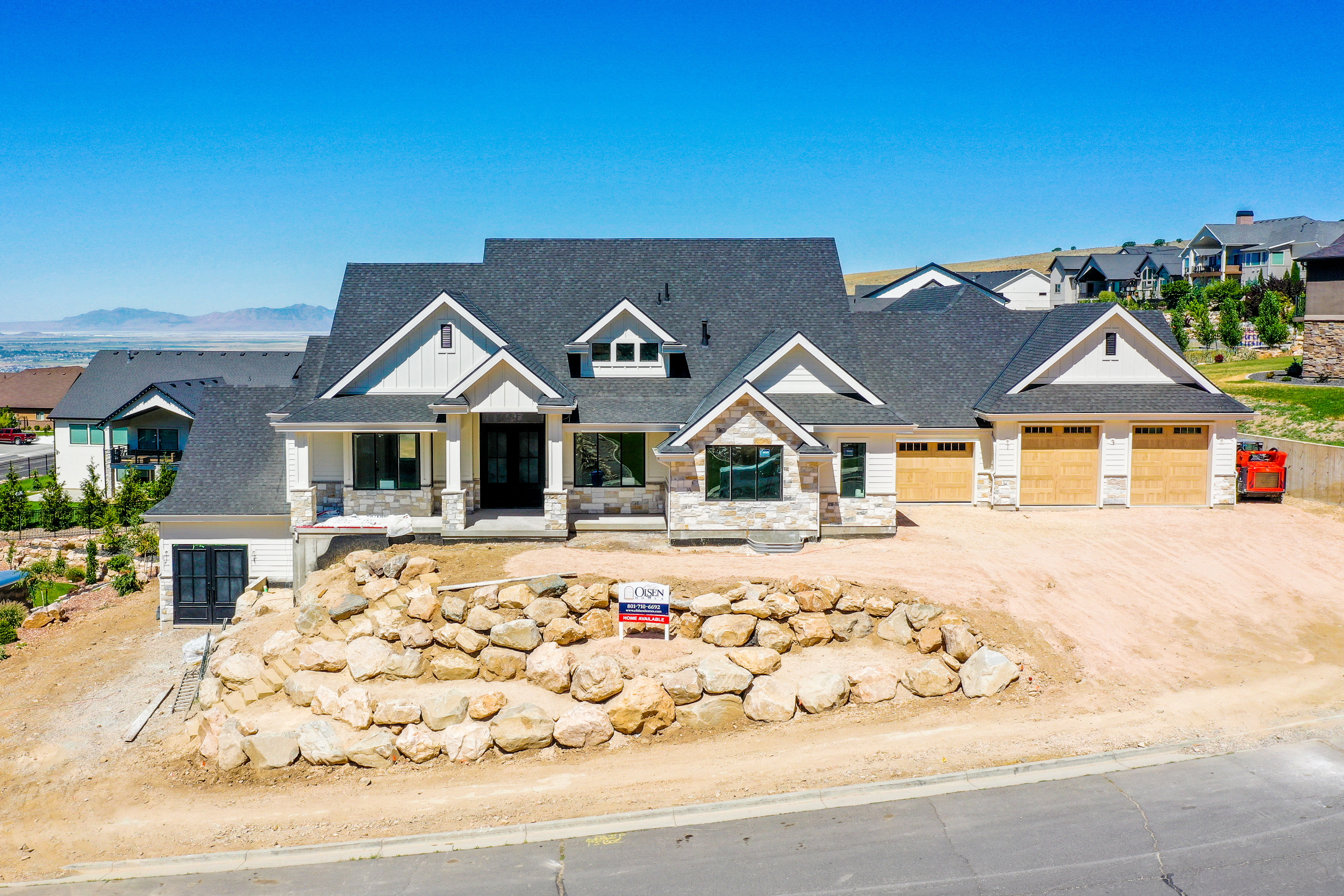 New construction residence featuring a multi-gable roofline, stone and siding exterior, and a three-car garage with wood-finish doors