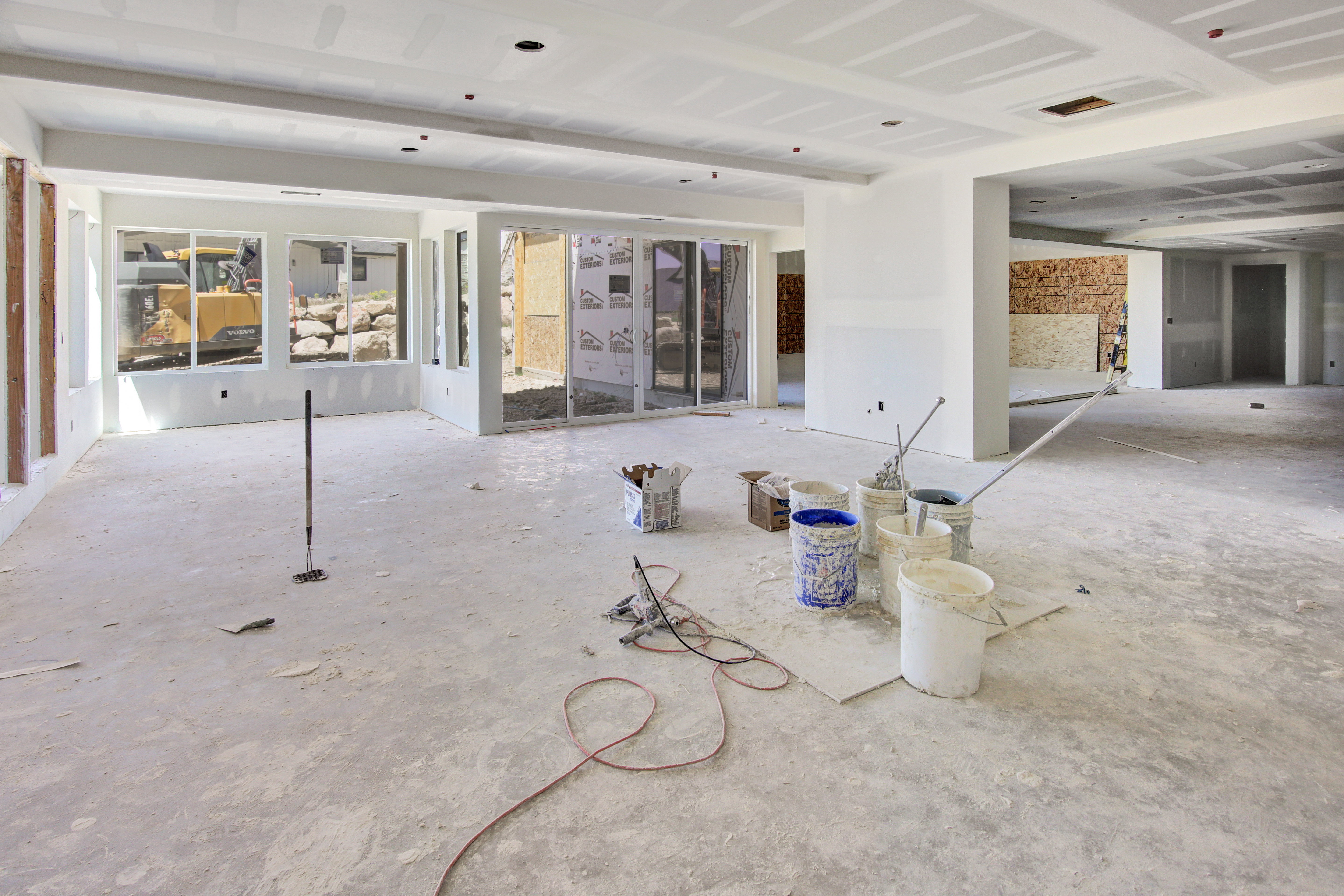 Spacious interior under construction featuring multiple large windows and sliding glass doors, high ceilings with recessed lighting, and an open floor plan