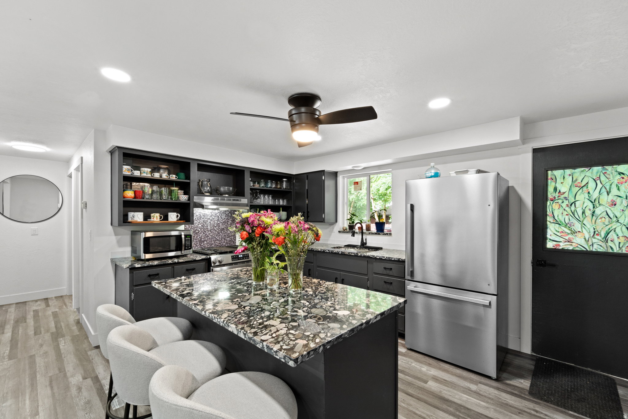 Contemporary kitchen featuring dark cabinetry, speckled countertops, stainless steel appliances, and wood-finish flooring
