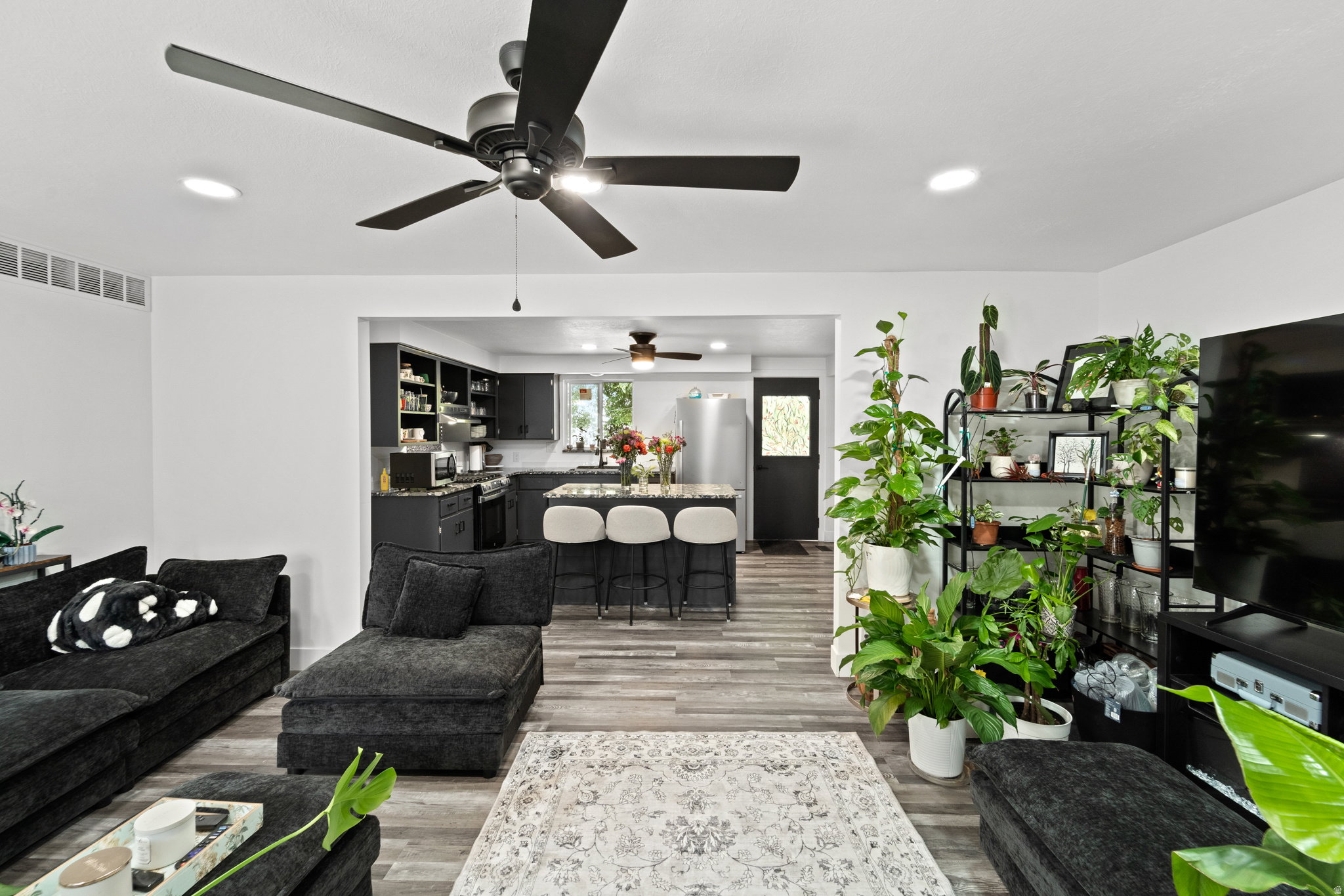 Open-concept living area featuring light wood-finish flooring, recessed lighting, and a black ceiling fan