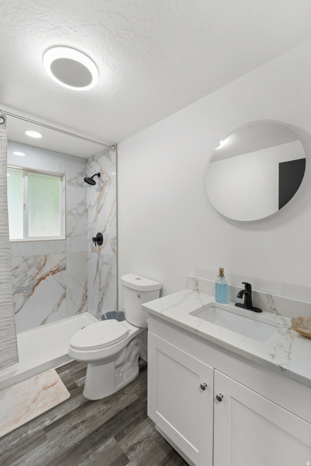 Bathroom featuring a white vanity with an integrated sink, black faucet, and a round frameless mirror