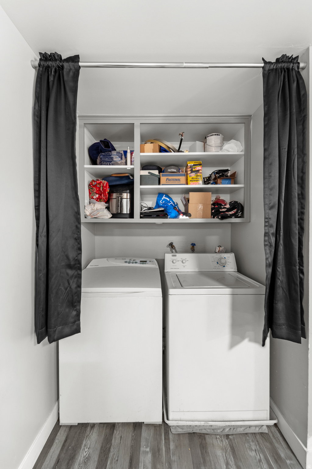 Dedicated laundry area featuring a built-in shelf unit, wood-finish flooring, white walls, and a clothes rod