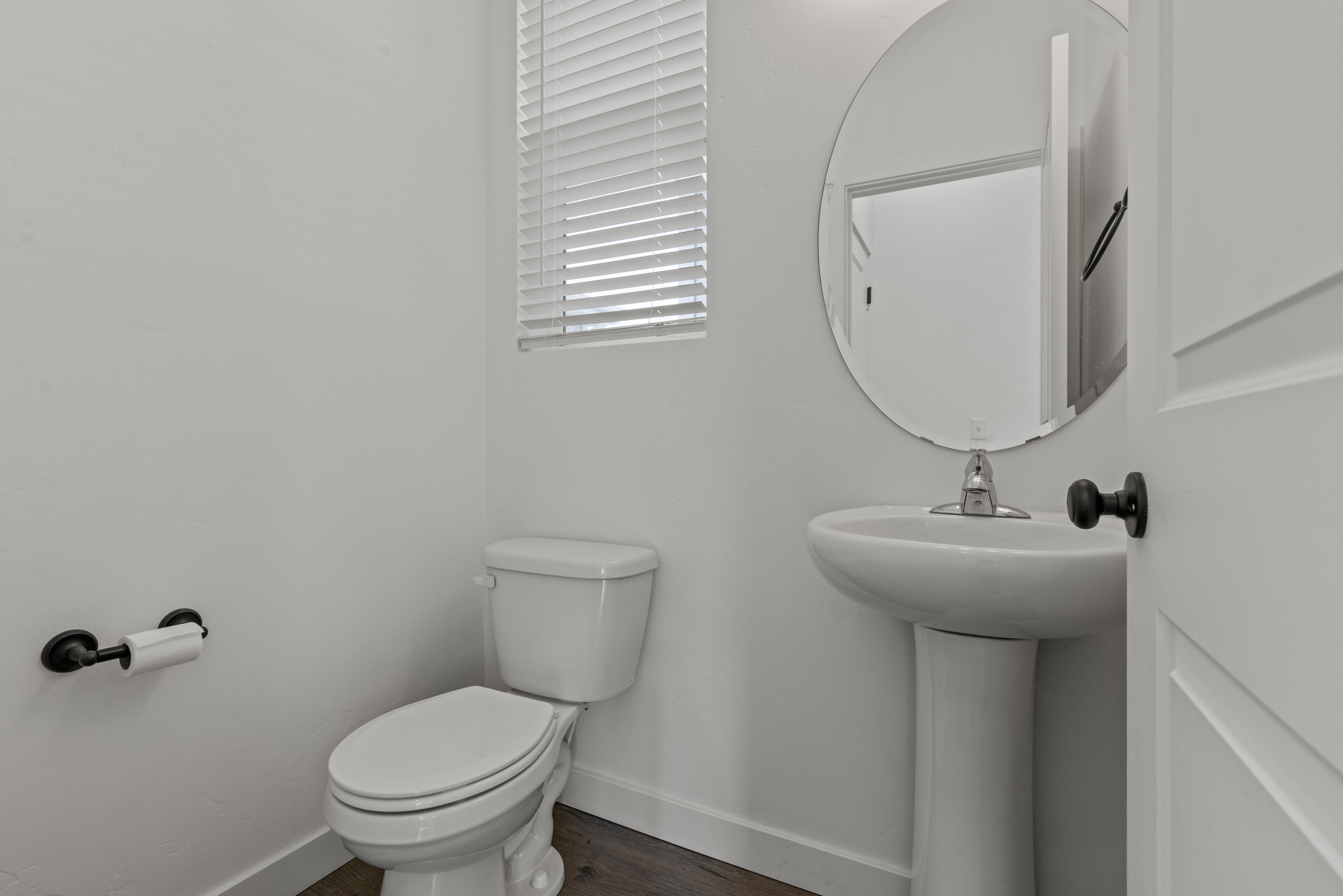 Powder room featuring a pedestal sink with a chrome faucet, an oval mirror, and wood-finish flooring