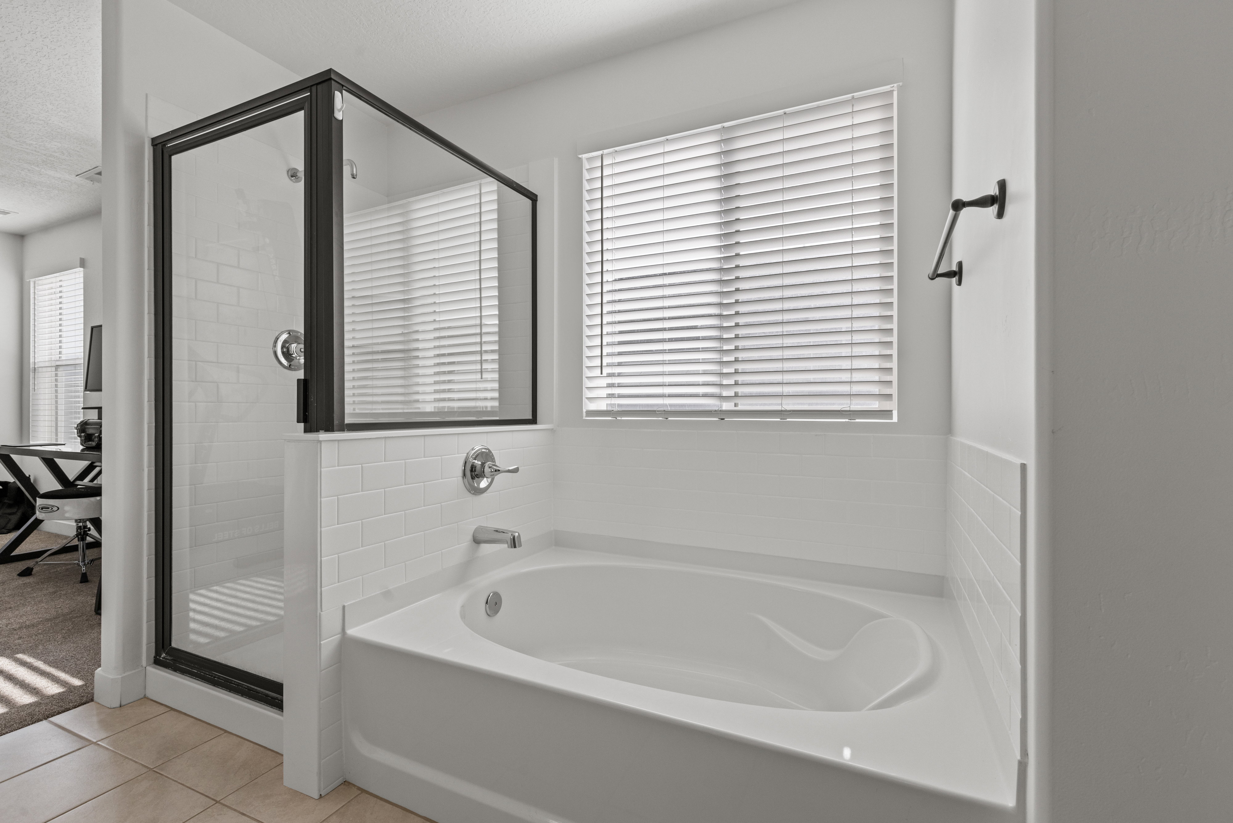 White soaking tub with subway tile surround, accompanied by a glass-enclosed shower with black framing