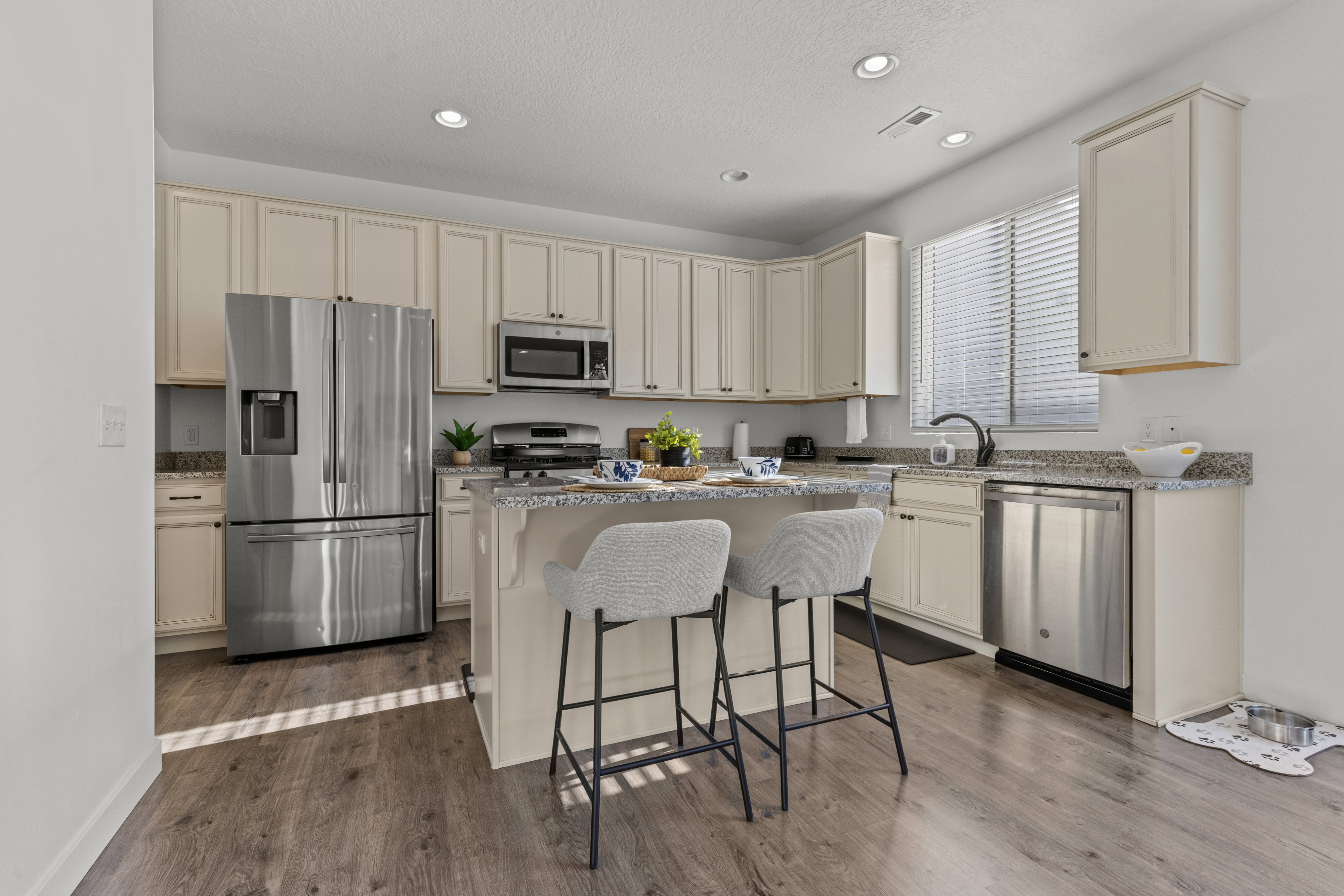 Kitchen featuring light wood-finish cabinetry, granite-style countertops, stainless steel appliances, a center island with built-in seating, and wood-finish flooring