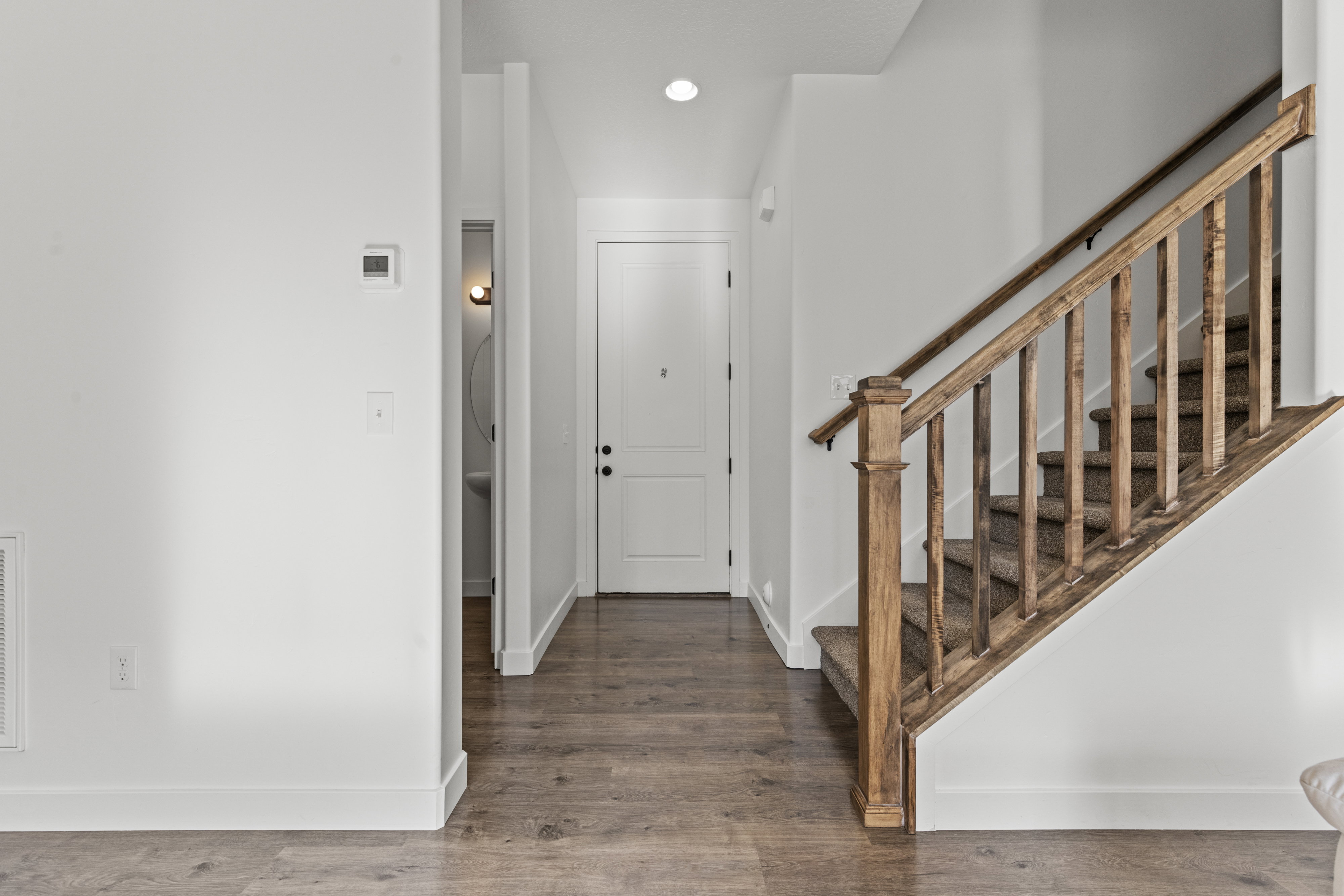 Entryway featuring wood-finish flooring, a wood staircase with carpeted treads, and a modern thermostat