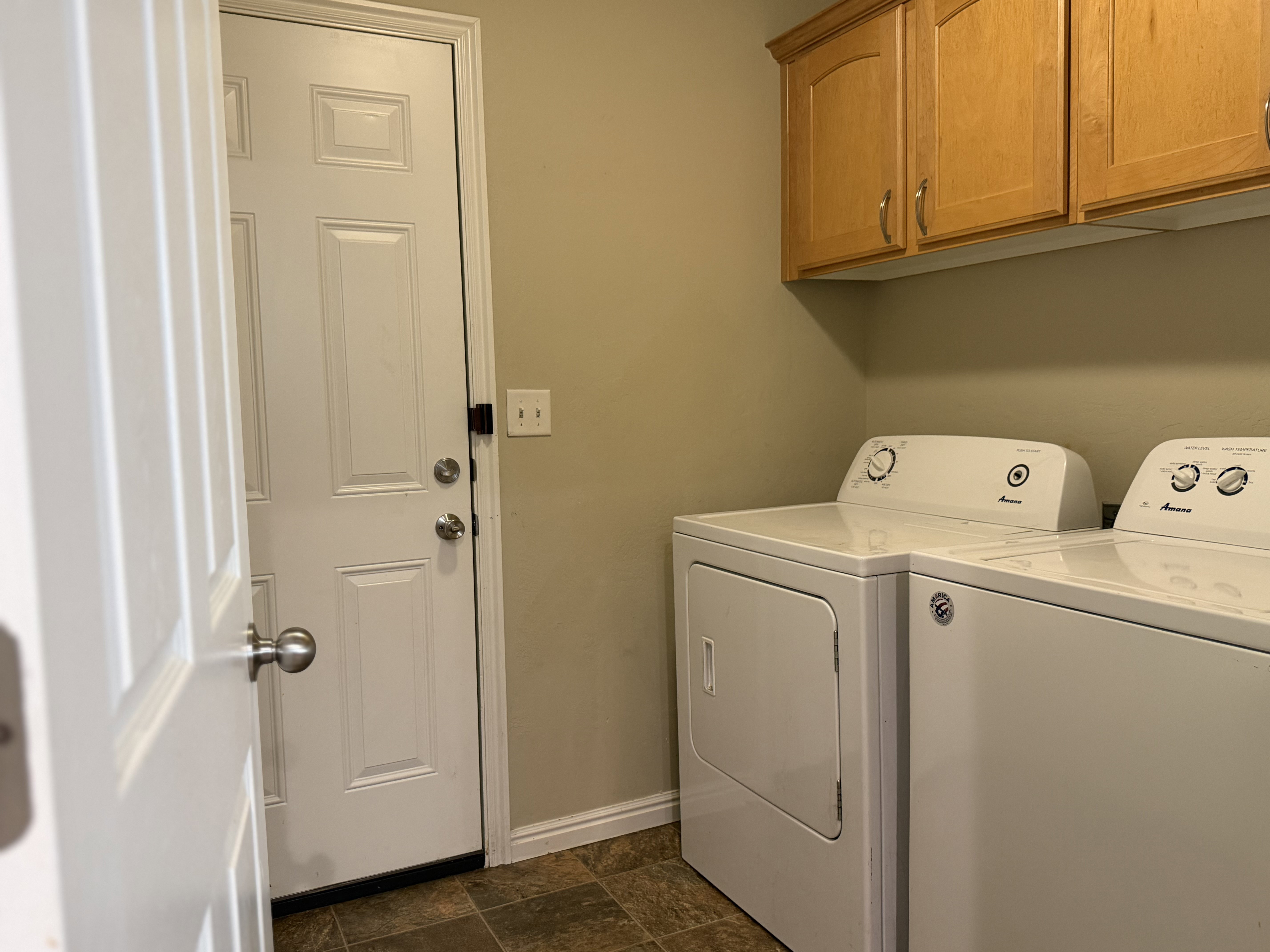 Laundry area featuring wood-finish cabinetry, neutral wall color, and brown tile-pattern flooring