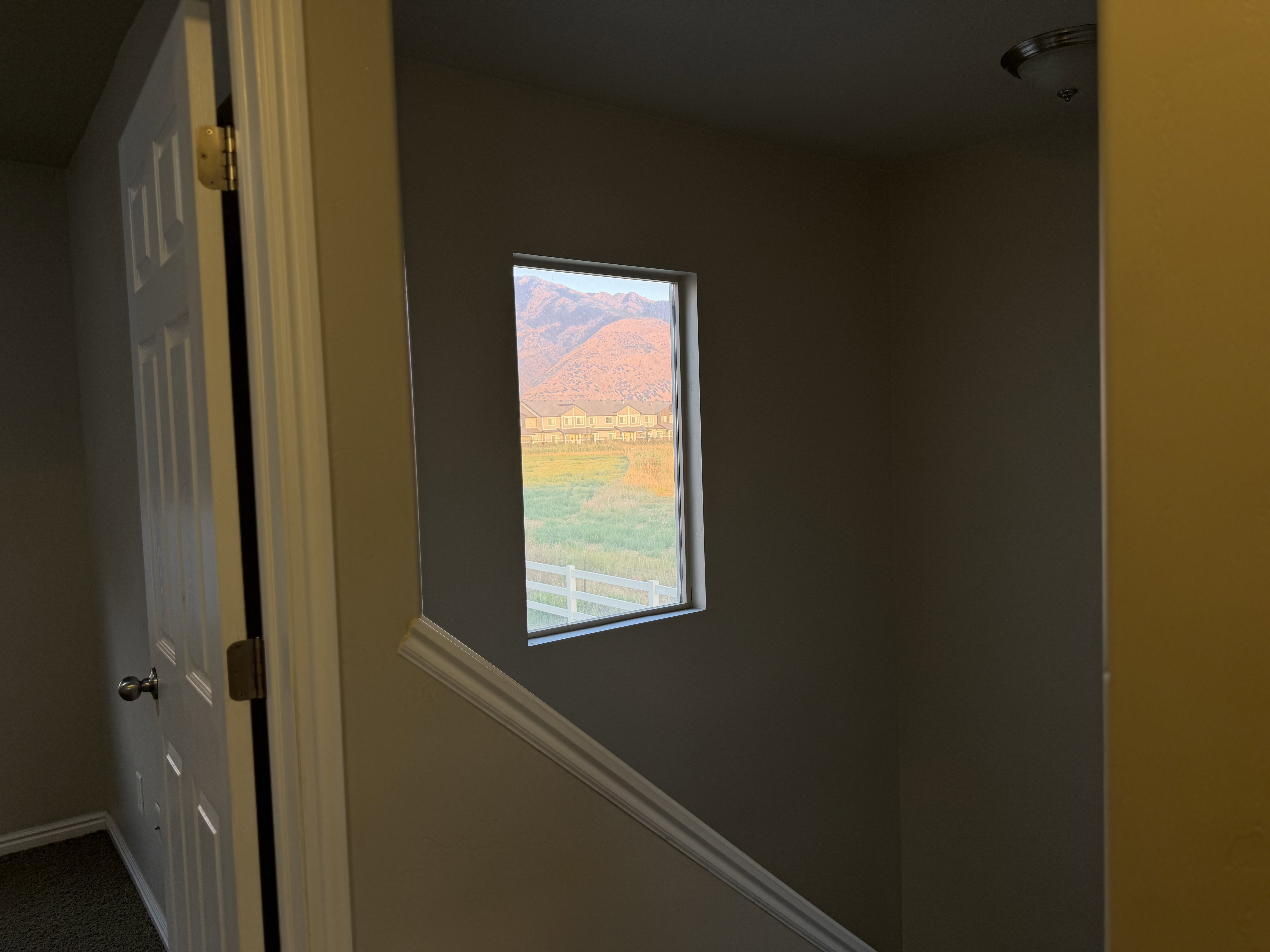 Window featuring a distant mountain range, open field, and white fence