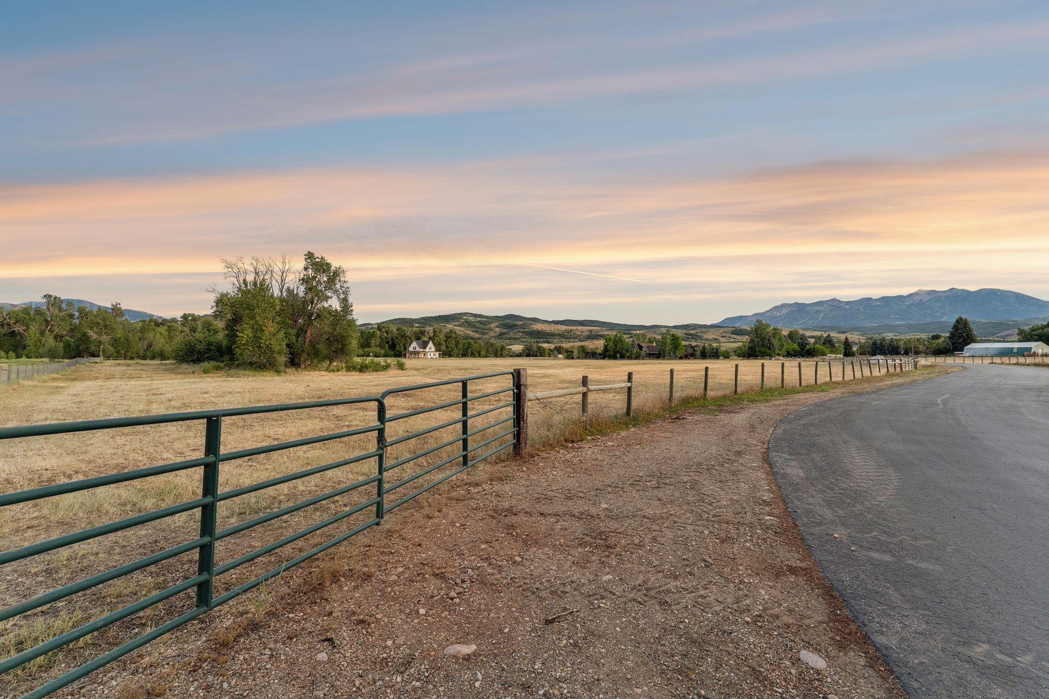 Expansive open field bordered by a metal fence and a paved road