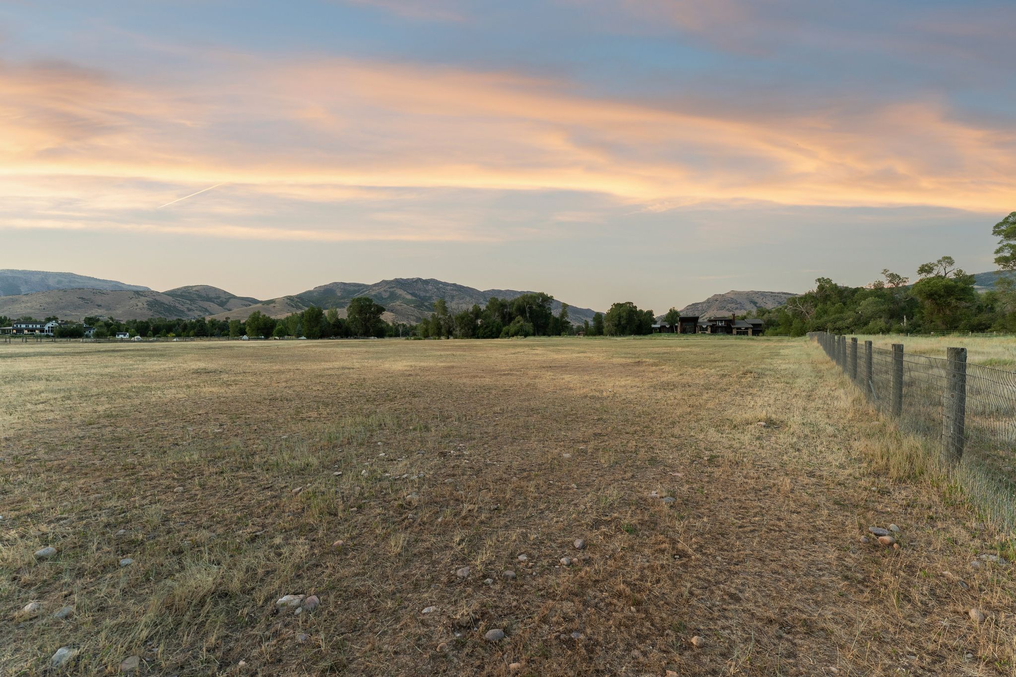 Expansive undeveloped land featuring a wire fence line, distant mountains, and scattered trees