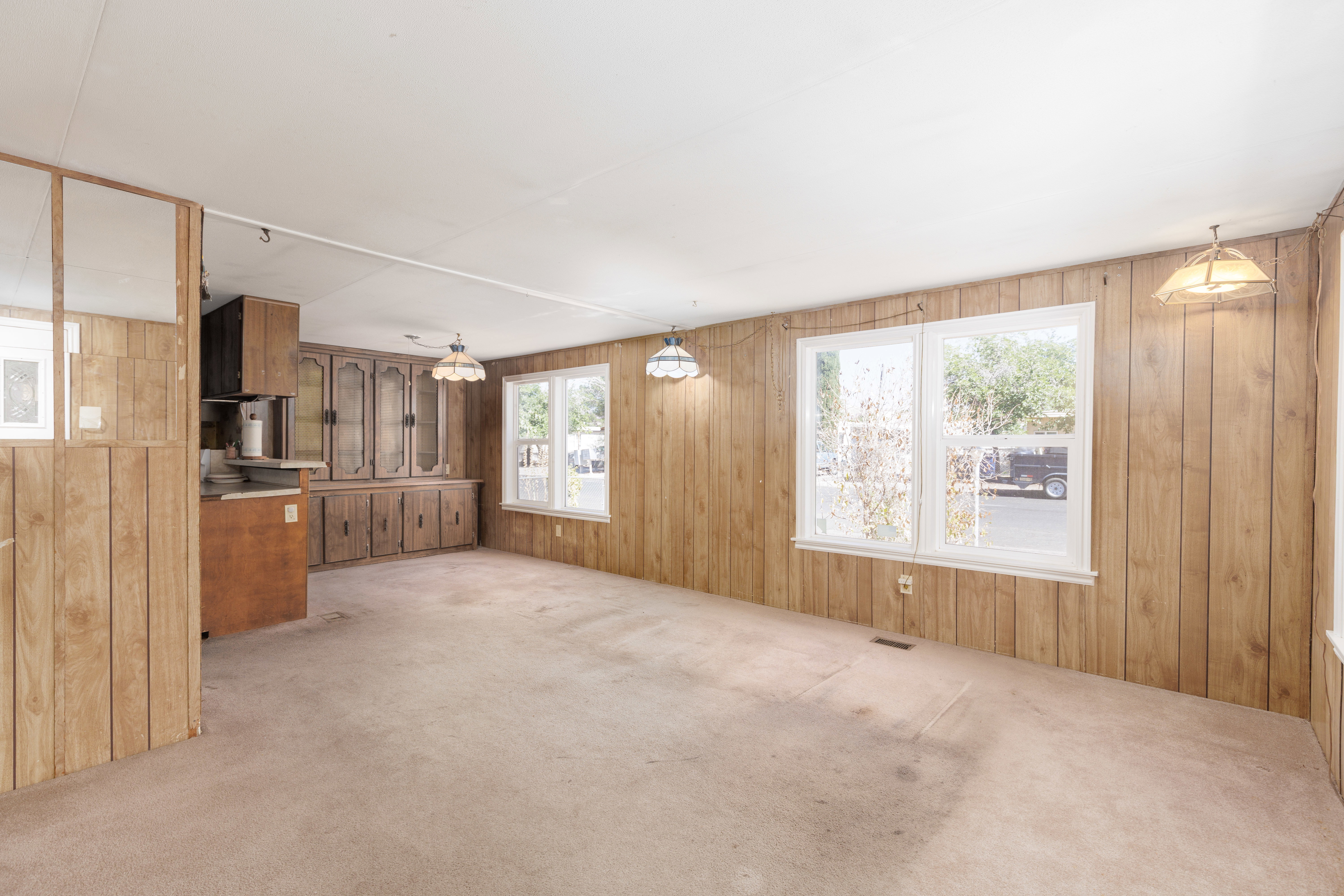 Spacious living area featuring light-colored carpet flooring and wood paneling