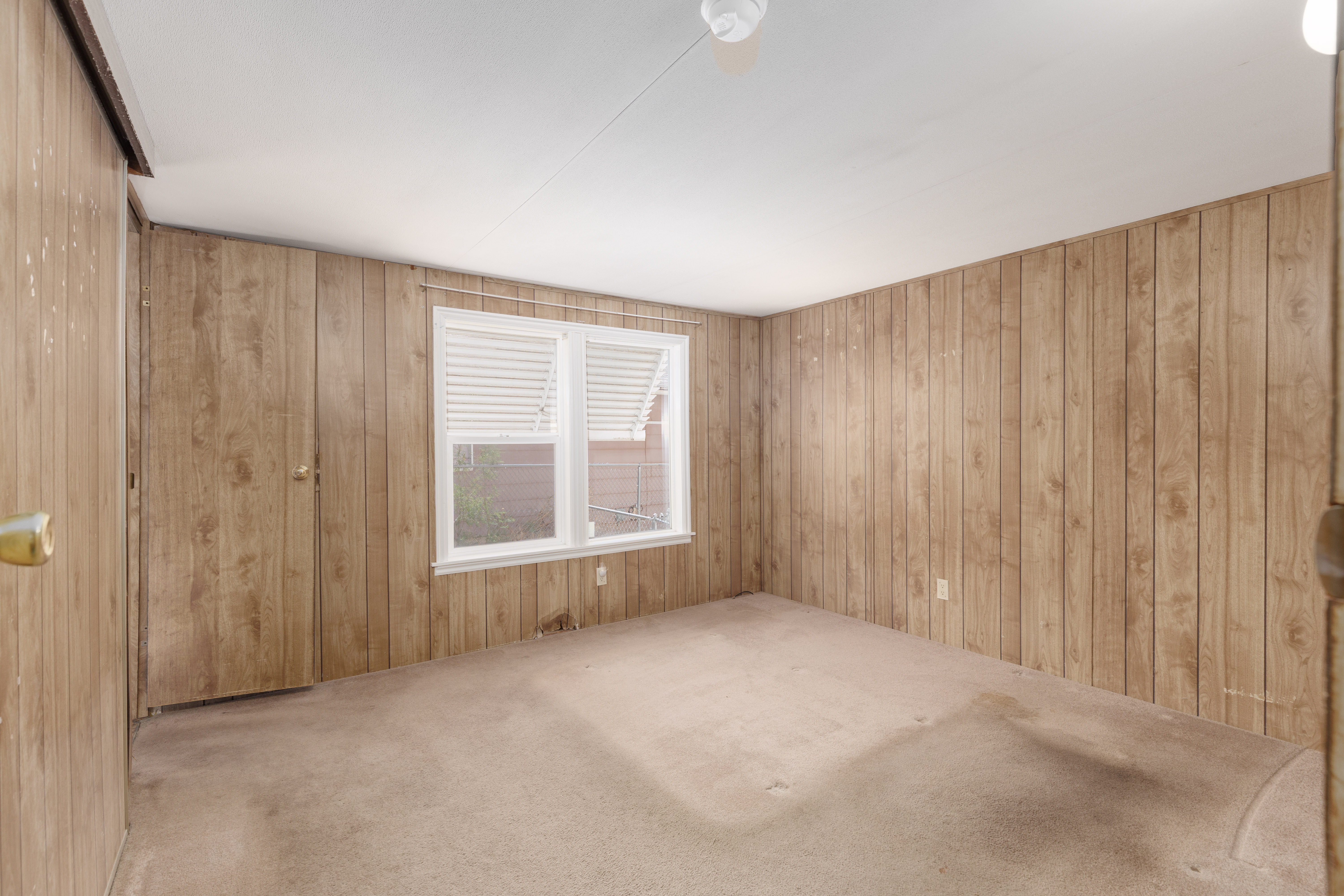 Room featuring wood-paneled walls, a double-hung window with blinds, and a built-in closet with double doors