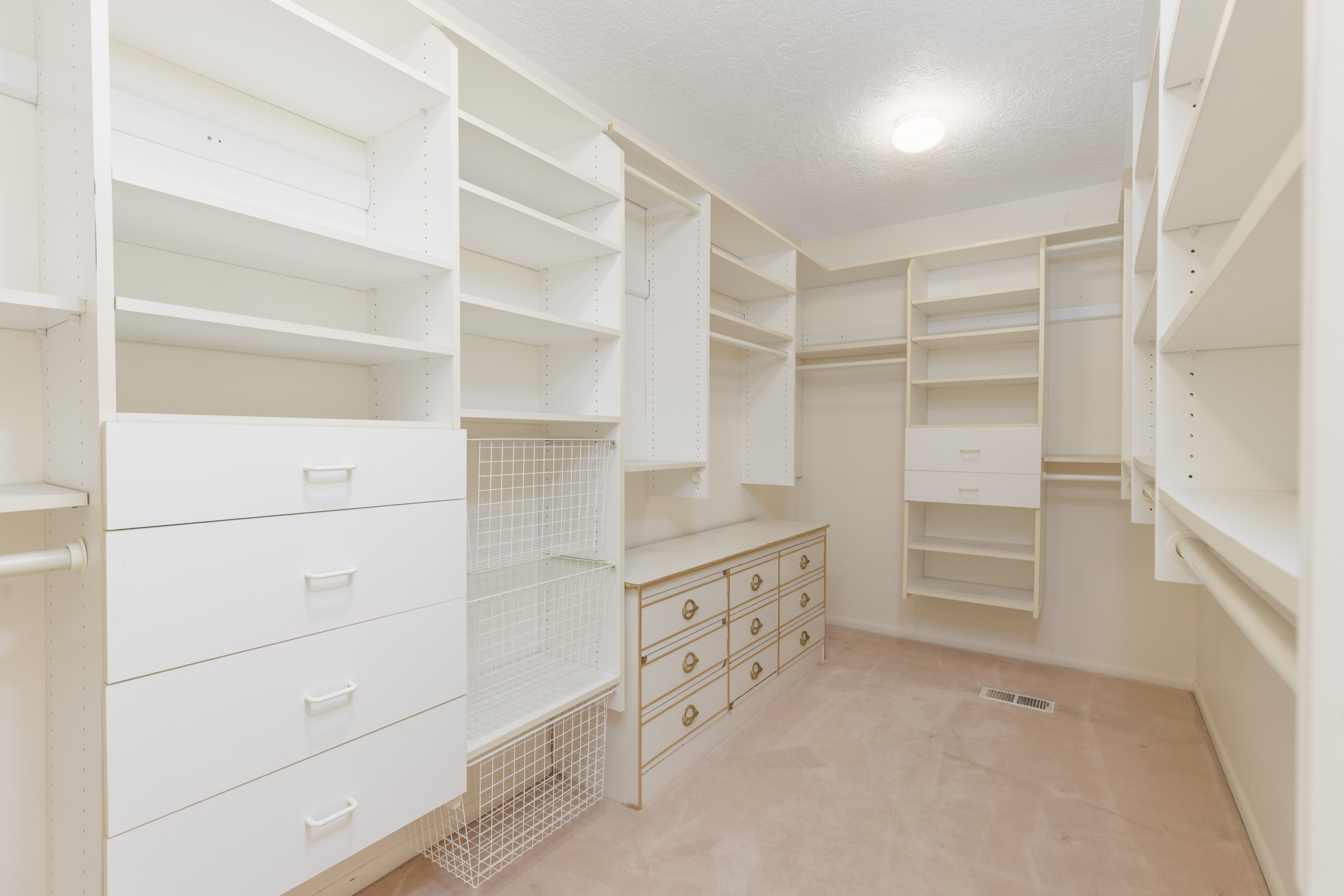 Expansive walk-in closet featuring white built-in shelving, integrated drawers, wire baskets, and multiple hanging rods