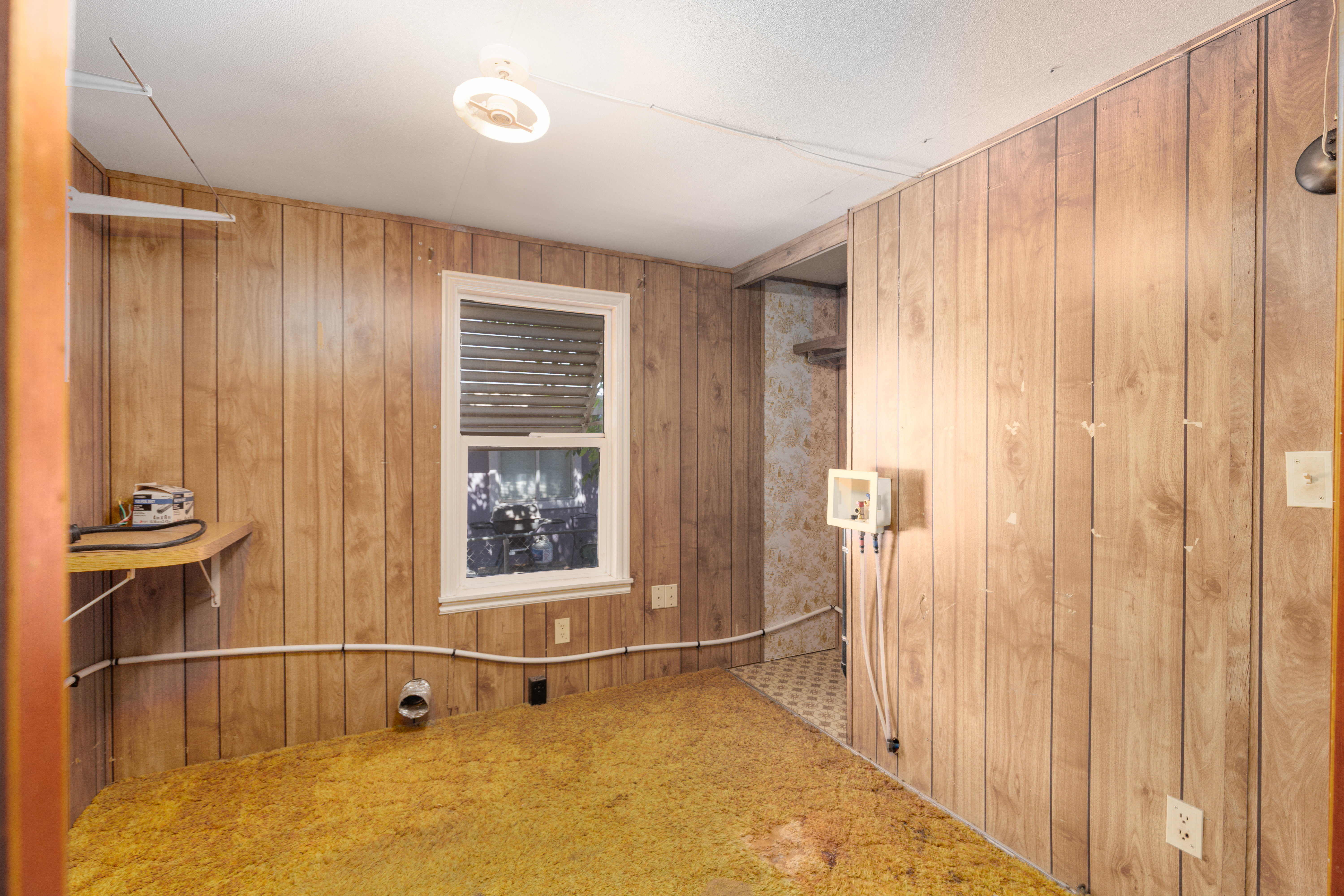 Room with wood-panel walls, a single-pane window, and a built-in shelf
