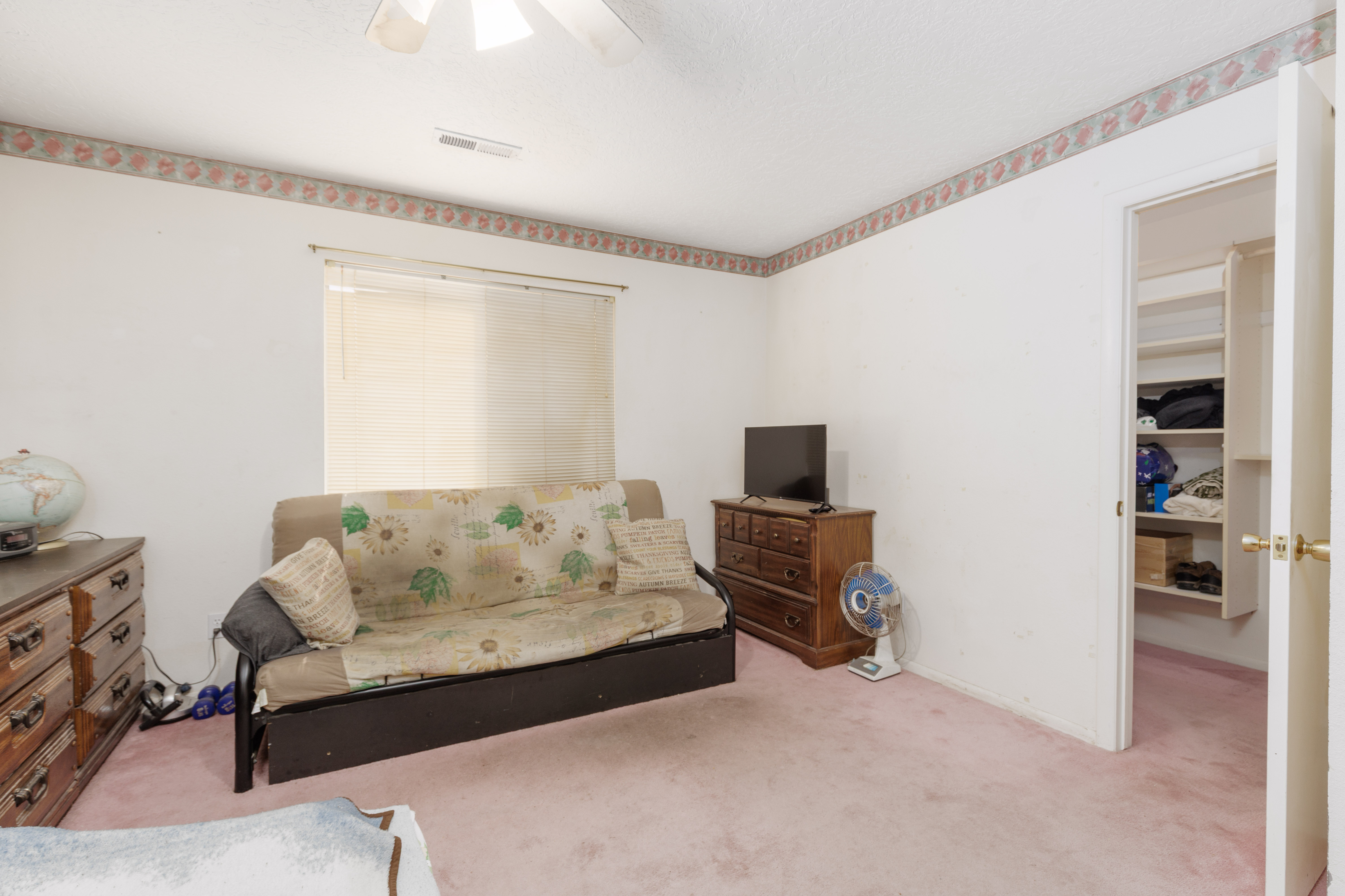 Carpeted room featuring a ceiling fan, a window with blinds, and an open closet with built-in shelving