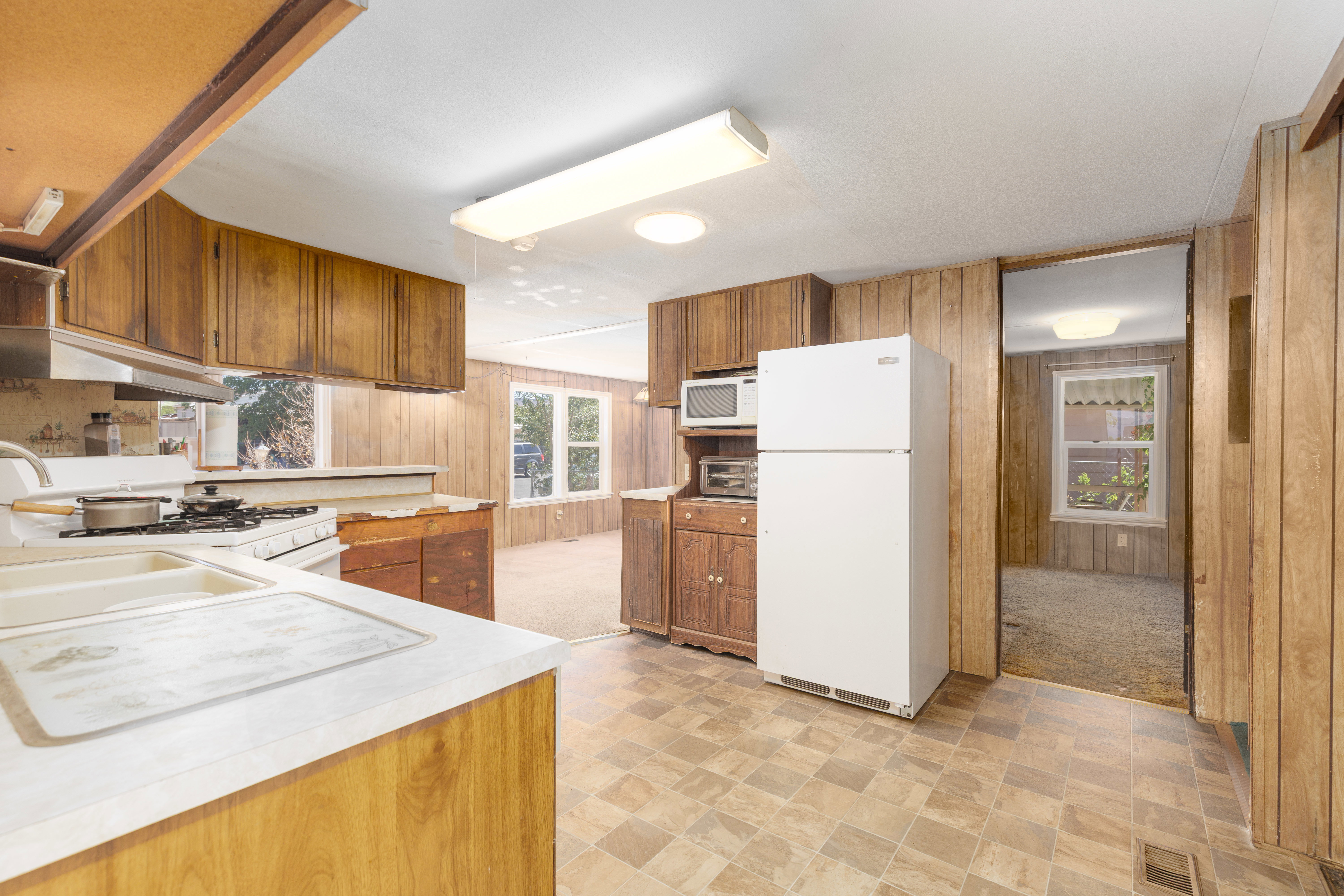 Kitchen featuring wood-finish cabinetry, white countertops, a four-burner gas range, white refrigerator, and vinyl flooring