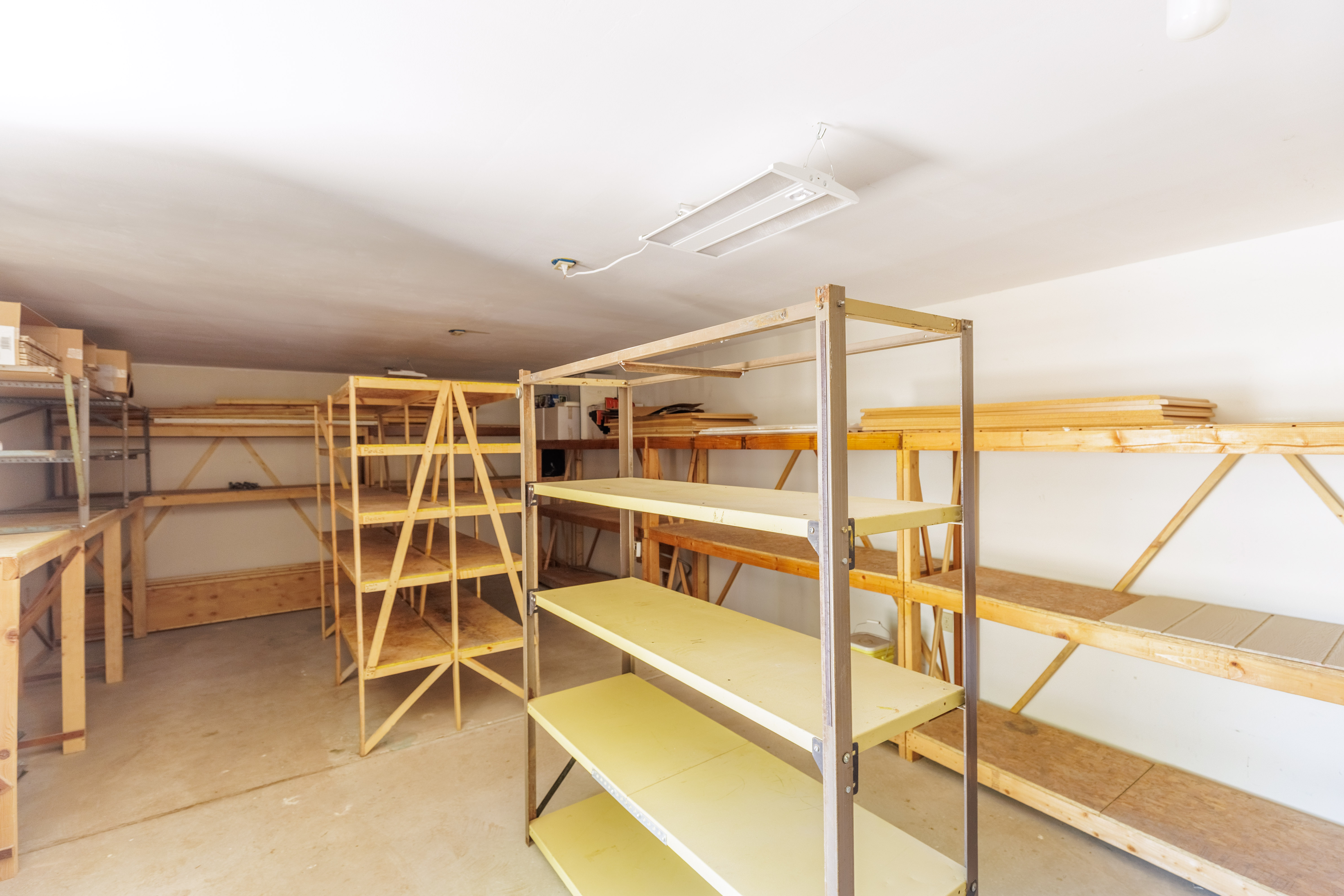 Spacious utility room featuring extensive built-in wooden shelving, a concrete floor, and fluorescent overhead lighting