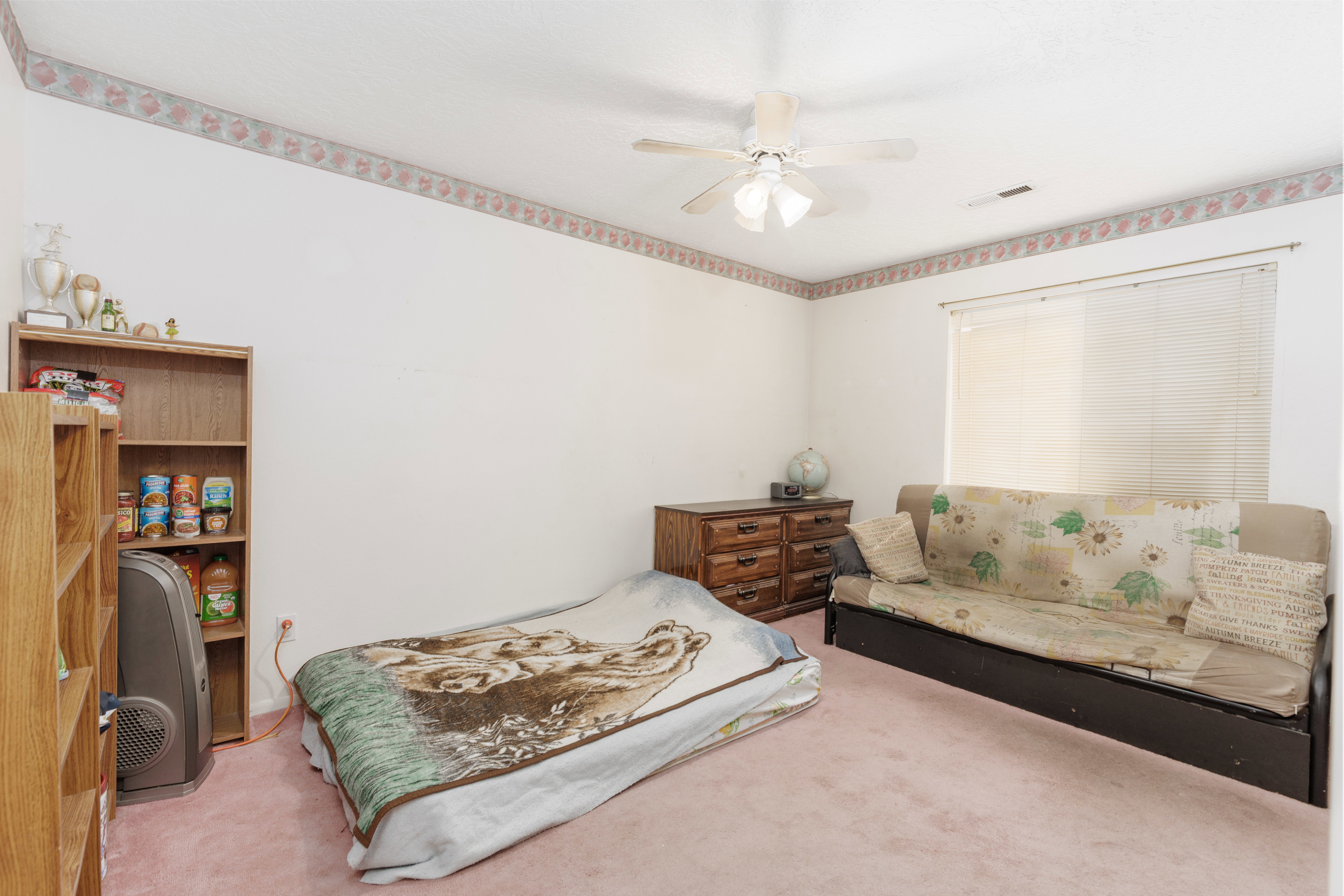 Carpeted room with a ceiling fan, a window with blinds, and white walls featuring a decorative border