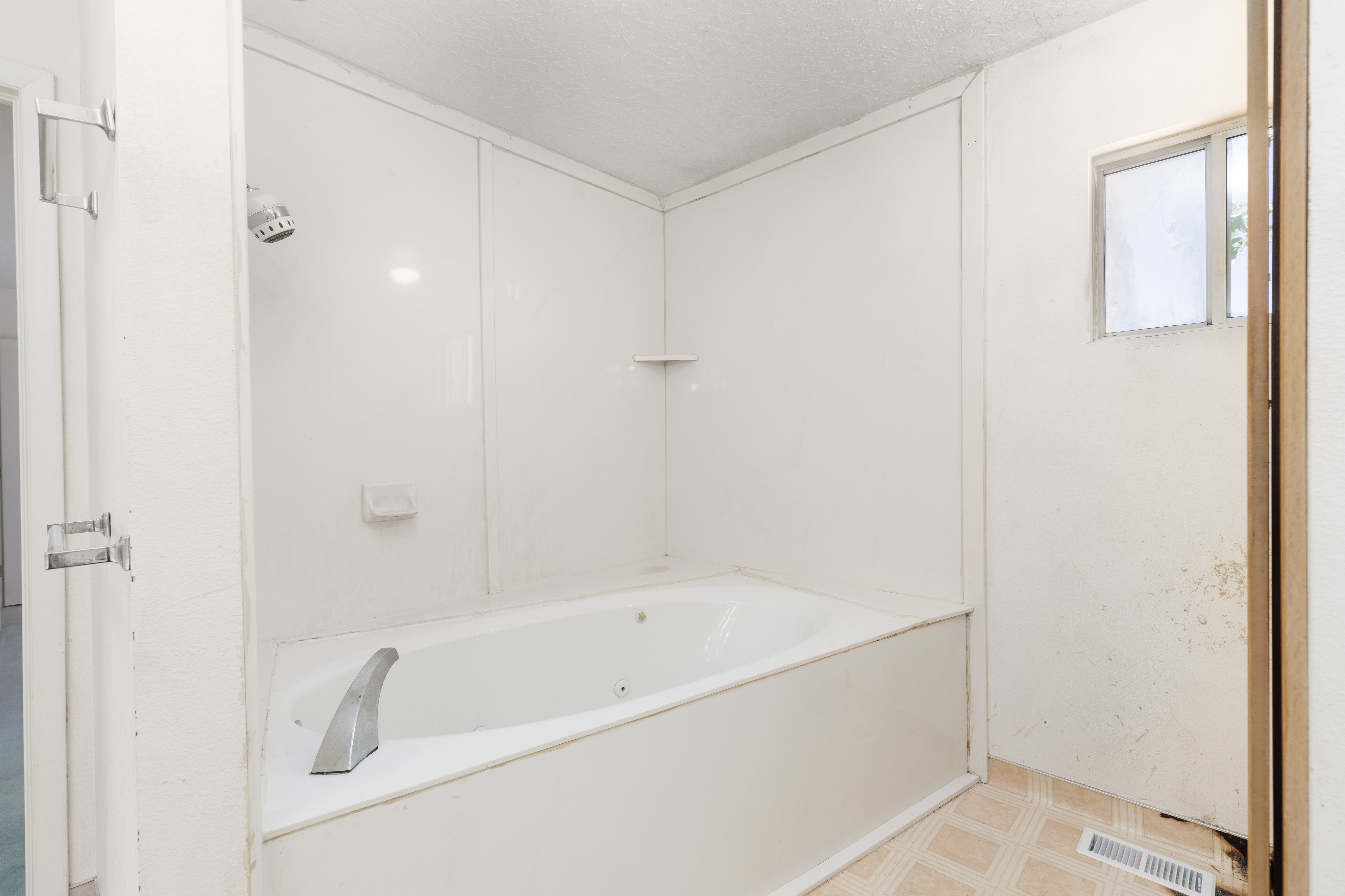 Built-in jetted tub with wall-mounted showerhead, integrated soap dish, and a small window