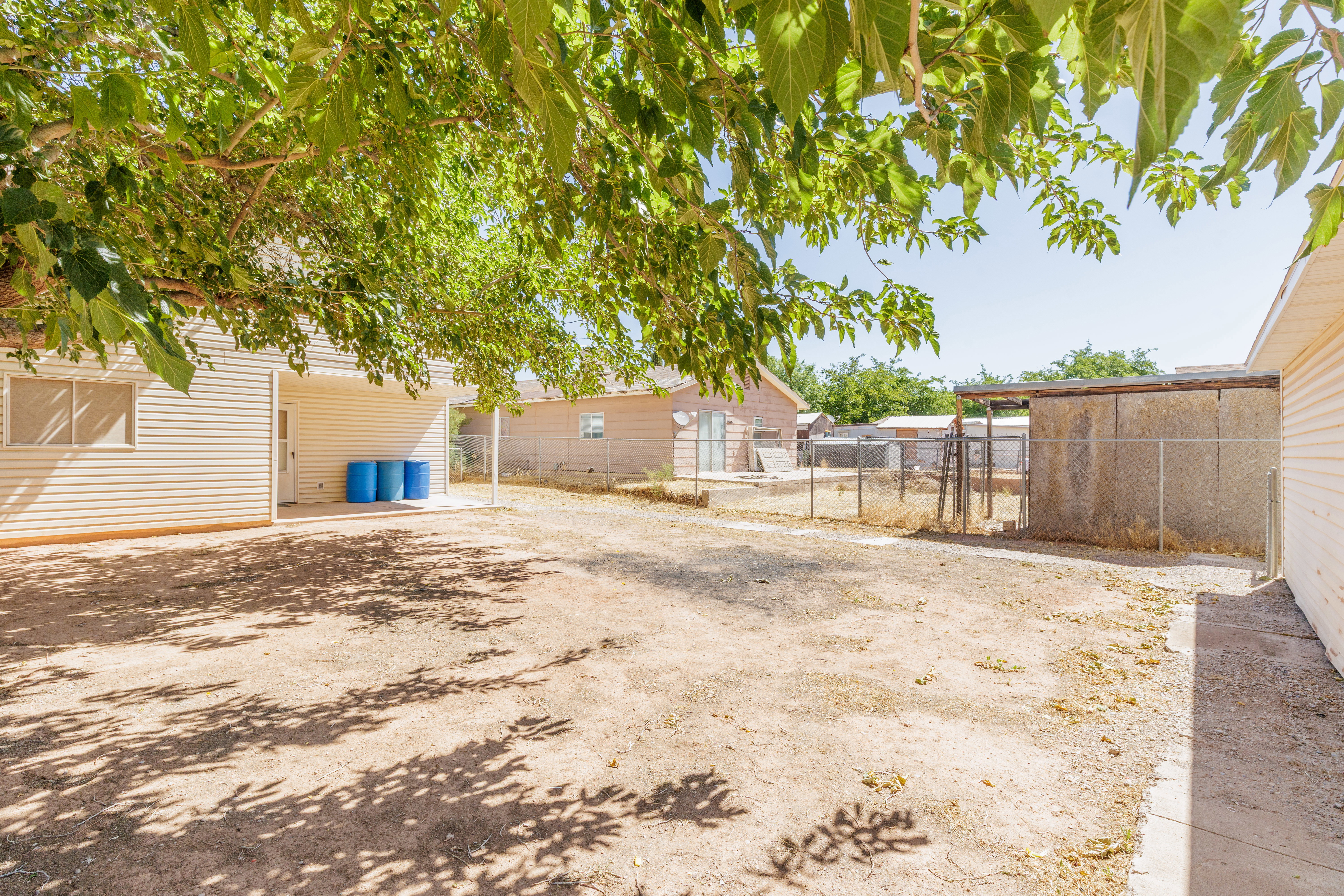 Expansive rear yard featuring a covered patio, mature tree, and a chain-link fence