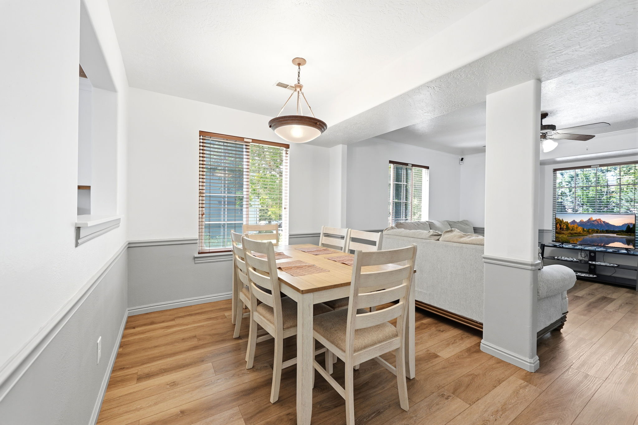Dining area featuring wood-finish flooring, a contemporary chandelier, a window with horizontal blinds, a pass-through opening to the left, and a half-wall partition