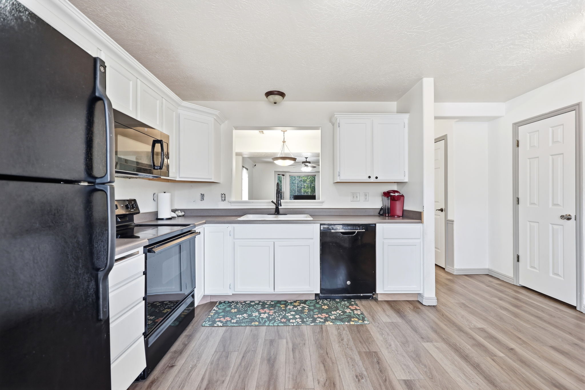 Kitchen featuring white cabinetry, wood-finish flooring, dark countertops, and a black appliance suite including a refrigerator, range, and dishwasher
