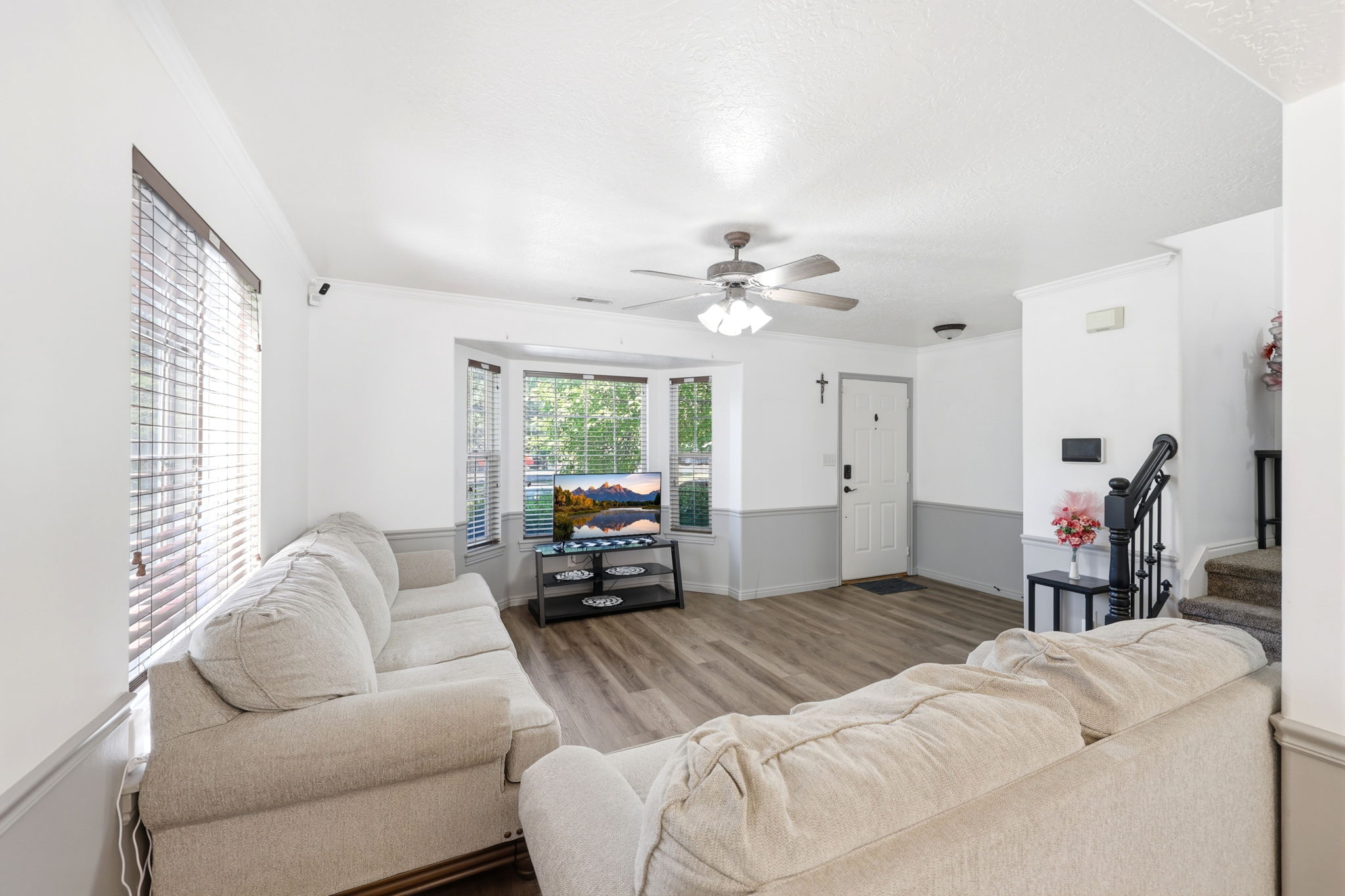 Spacious living area featuring wood-finish flooring, a bay window, and a ceiling fan with integrated lighting