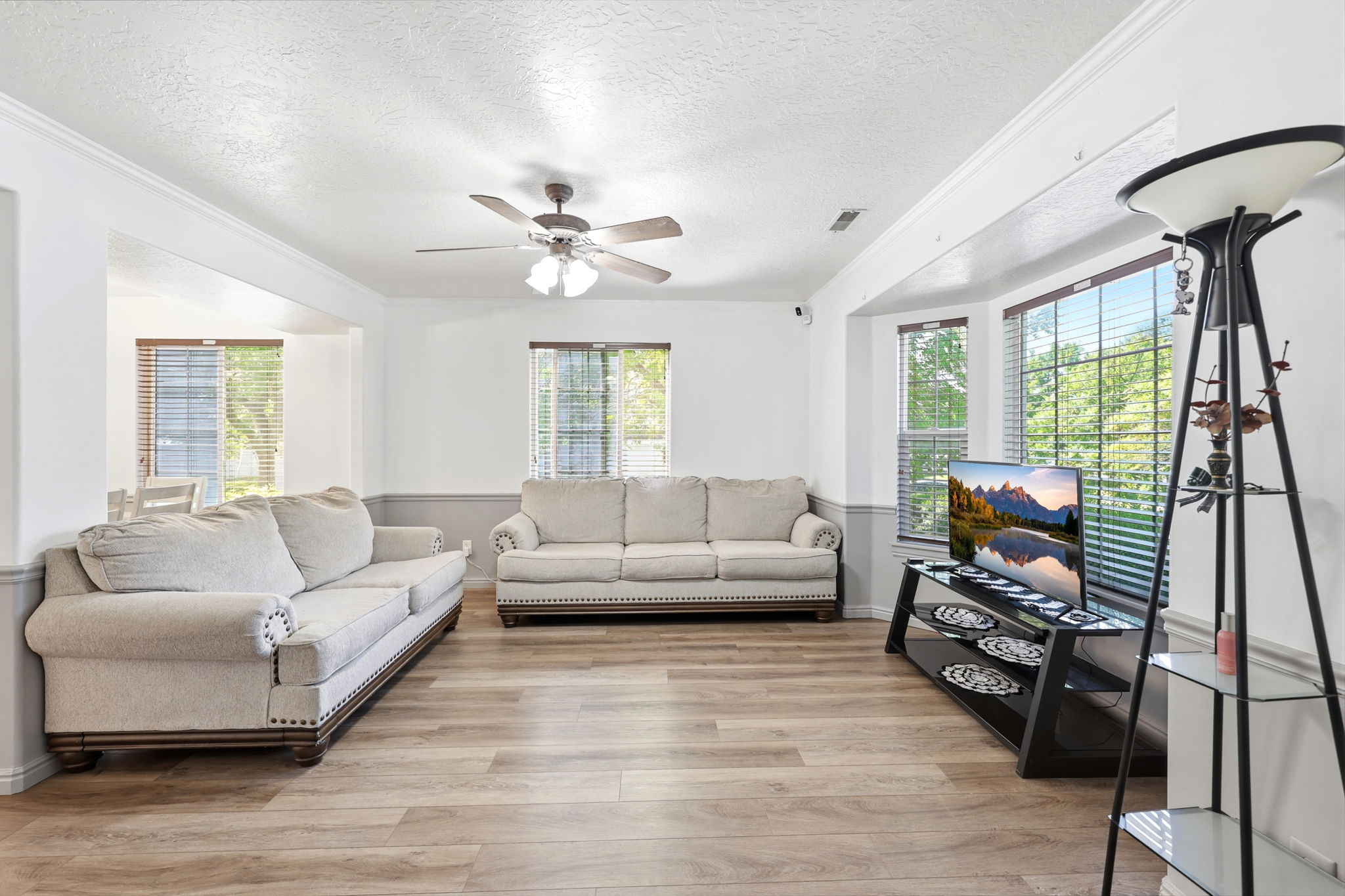 Living area featuring wood-finish flooring, a ceiling fan, crown molding, and a bay window