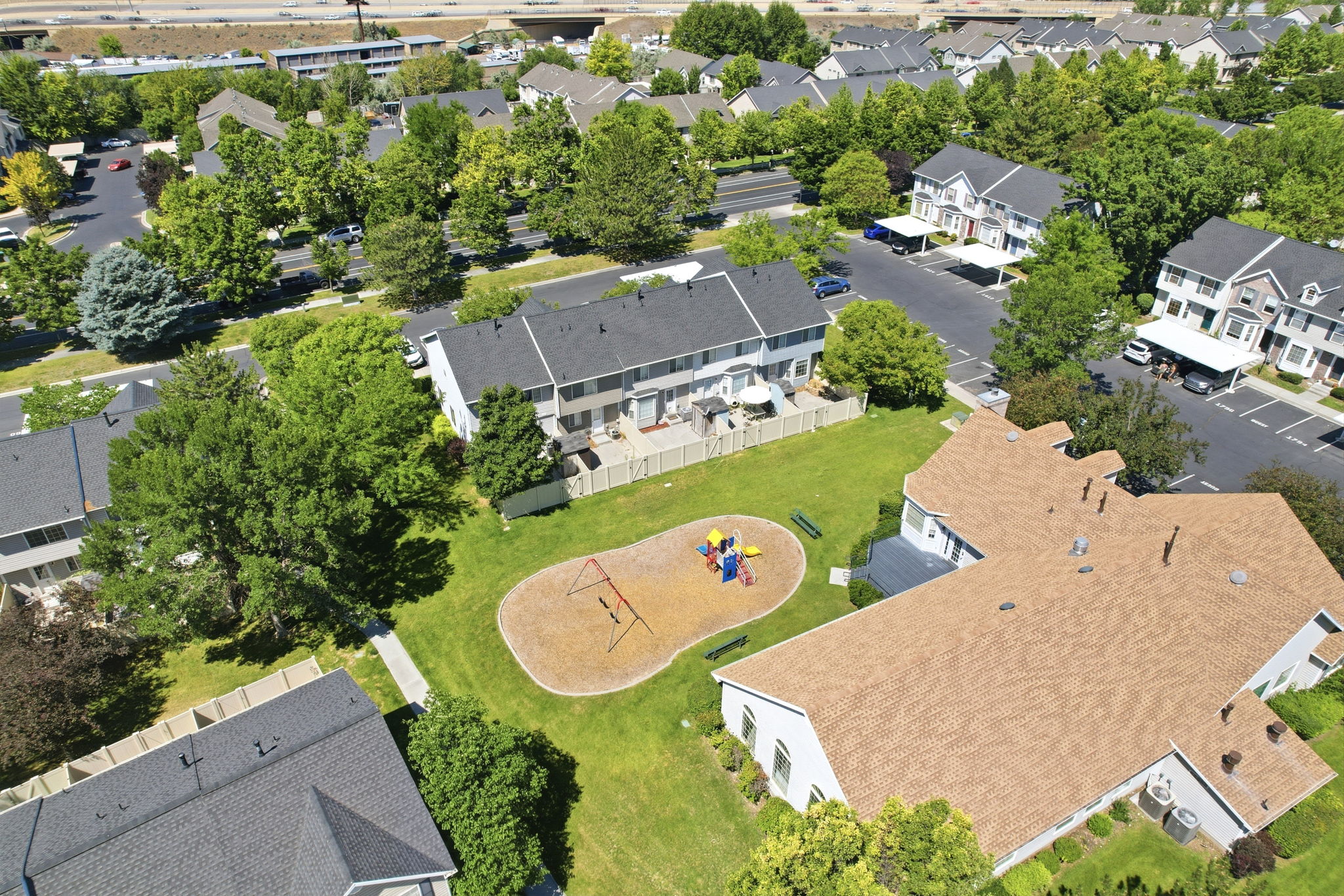 Expansive green space featuring a playground with swing set and slide, surrounded by a manicured lawn and mature trees