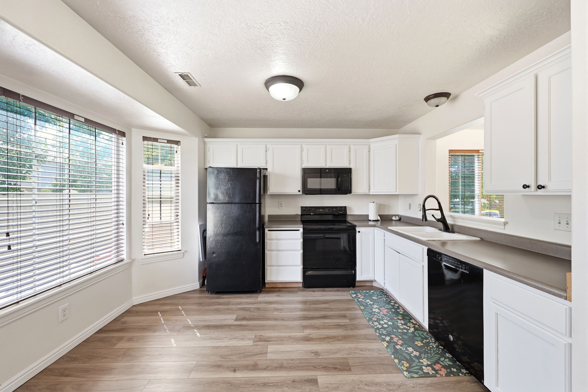 Kitchen featuring white cabinetry, dark countertops, black appliances, and wood-finish flooring